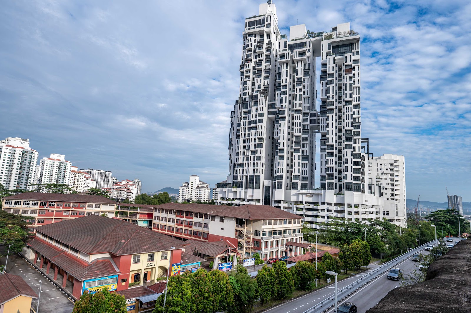 Icon Residence: Distinctive high-rise residential towers with cutout architectural gaps, surrounded by other buildings and low-rise shophouses in the foreground with a road and trees