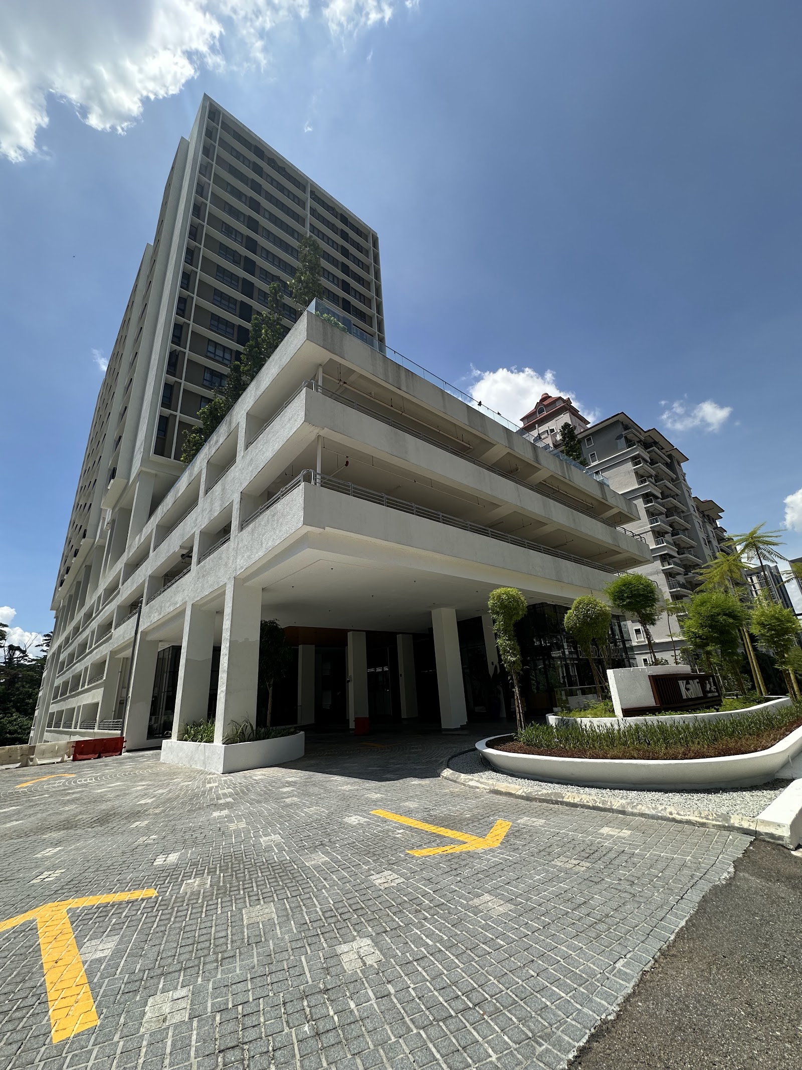 Kami: Exterior view of a high-rise residential building with parking podium levels and landscaped entrance driveway