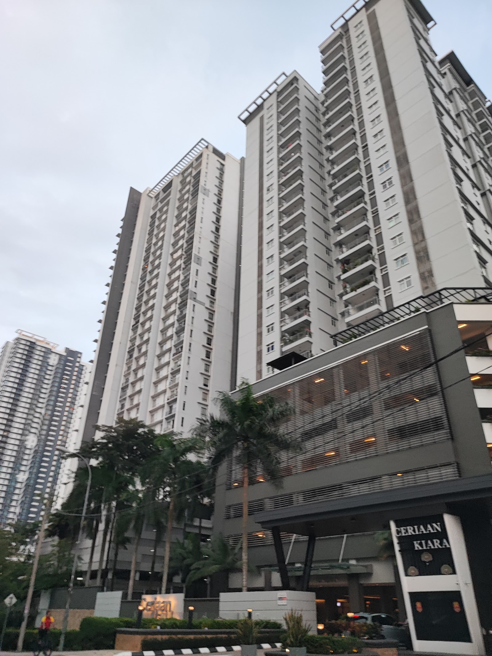 Ceriaan Kiara: View of tall residential towers with balconies, entrance signage reading 'Ceriaan Kiara', palm trees and driveway in front
