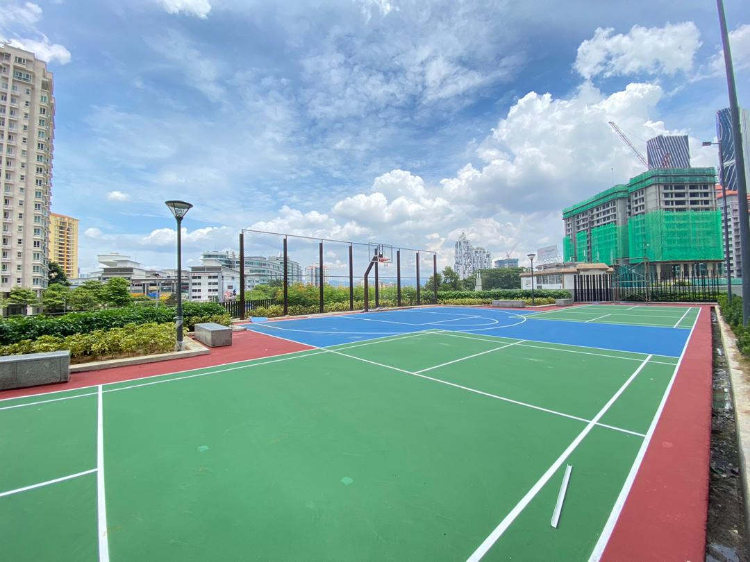 Agile Mont Kiara: A rooftop multi-purpose sports court with basketball hoop, painted in green, blue and red, surrounded by city buildings under a partly cloudy sky