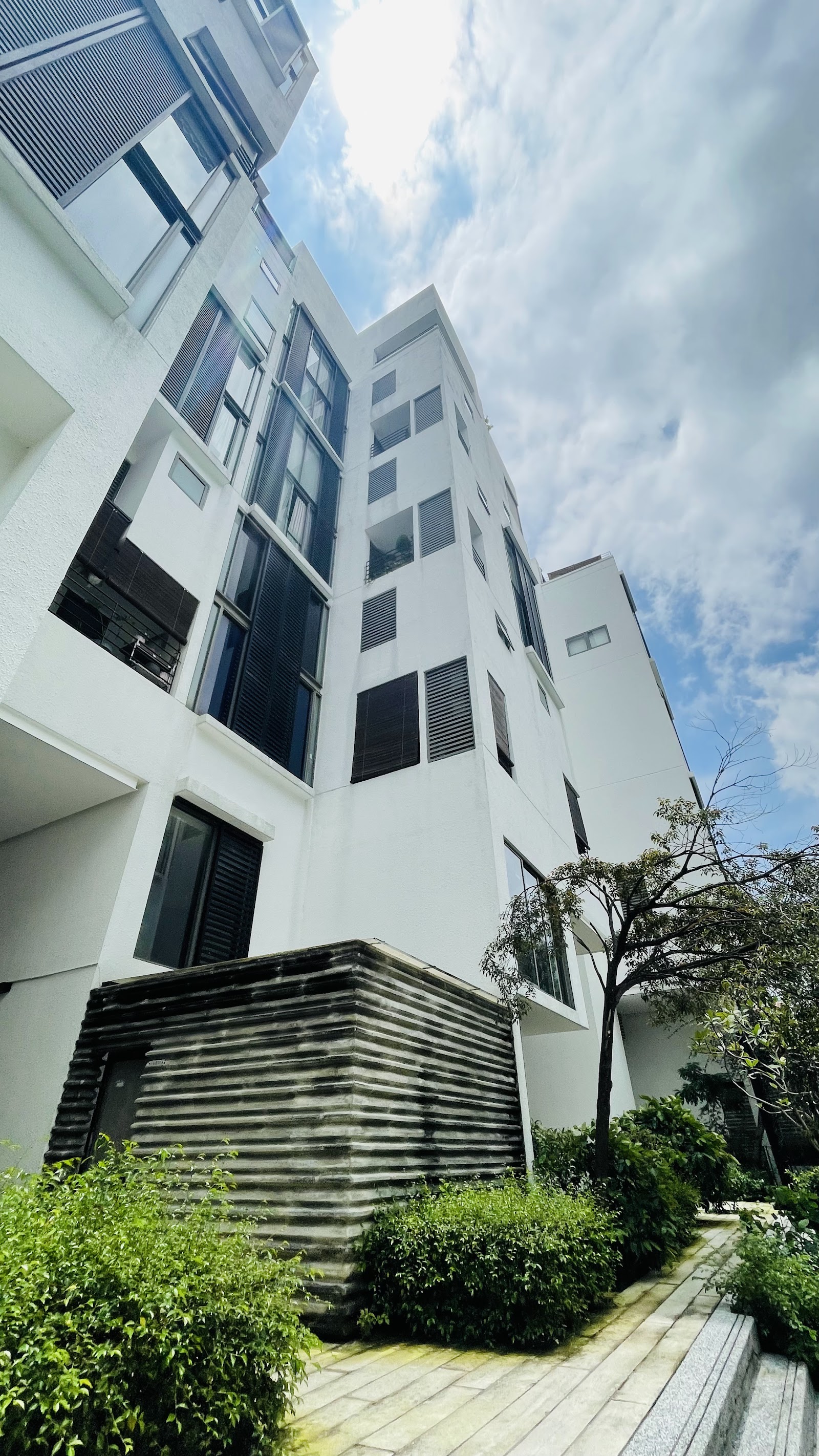 Centrio: Low-angle view of a modern white residential building facade with dark window shutters, surrounded by greenery
