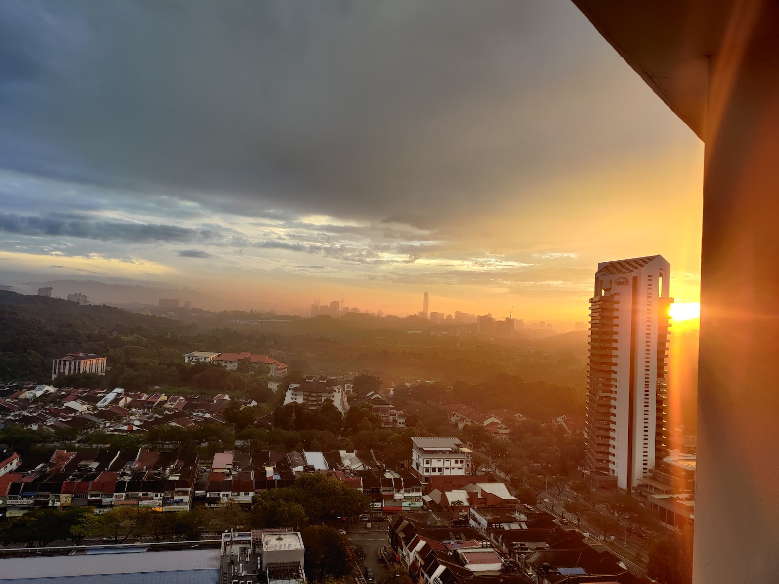 Sinaran TTDI: Sunset skyline view from a high-rise balcony overlooking a residential neighborhood, trees, a nearby tower, and distant city skyline