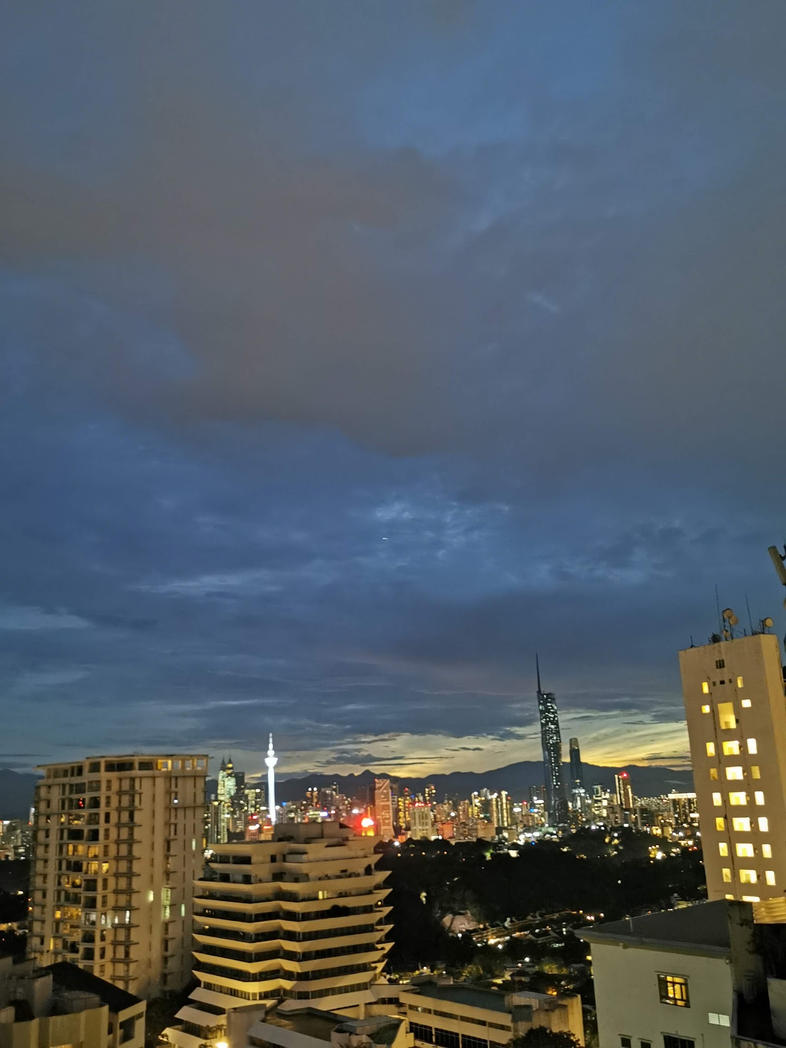 Araville: Night skyline view from a high-rise balcony showing city towers, a telecommunications tower, and dramatic sunset clouds