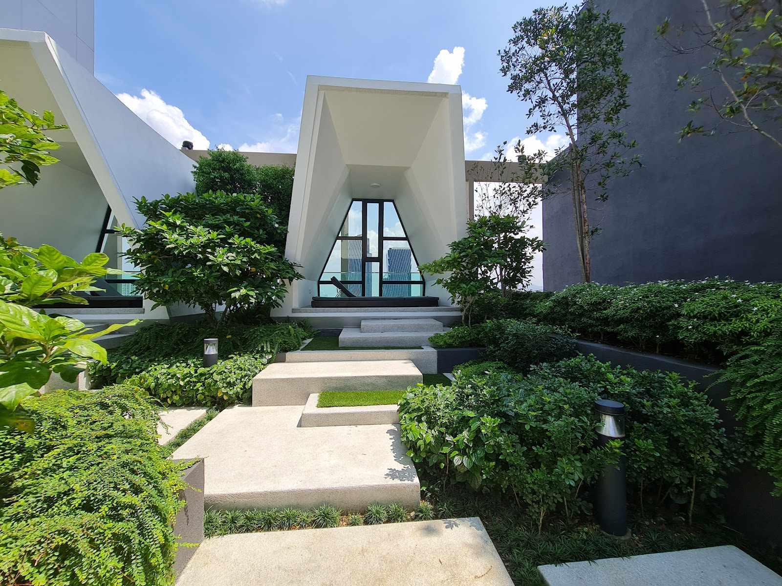 Residensi Solaris Parq: A landscaped garden pathway leading to a modern architectural pavilion with a triangular glass window overlooking city skyscrapers