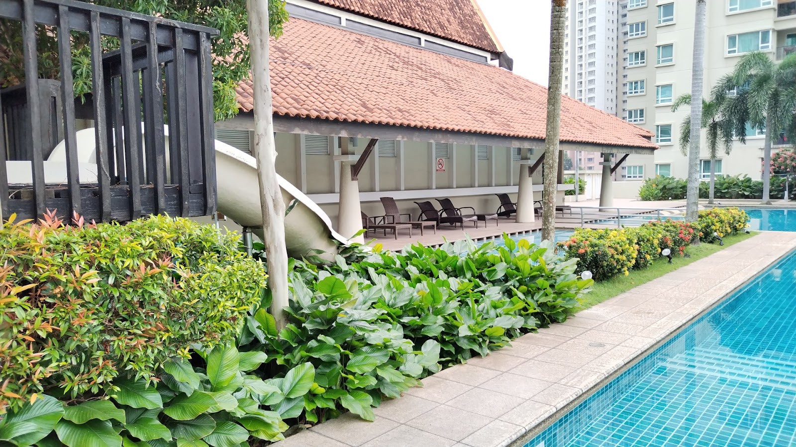 Mont Kiara Banyan: Swimming pool area with lounge chairs, slide, and landscaped garden beside a covered pavilion, with high-rise buildings in the background
