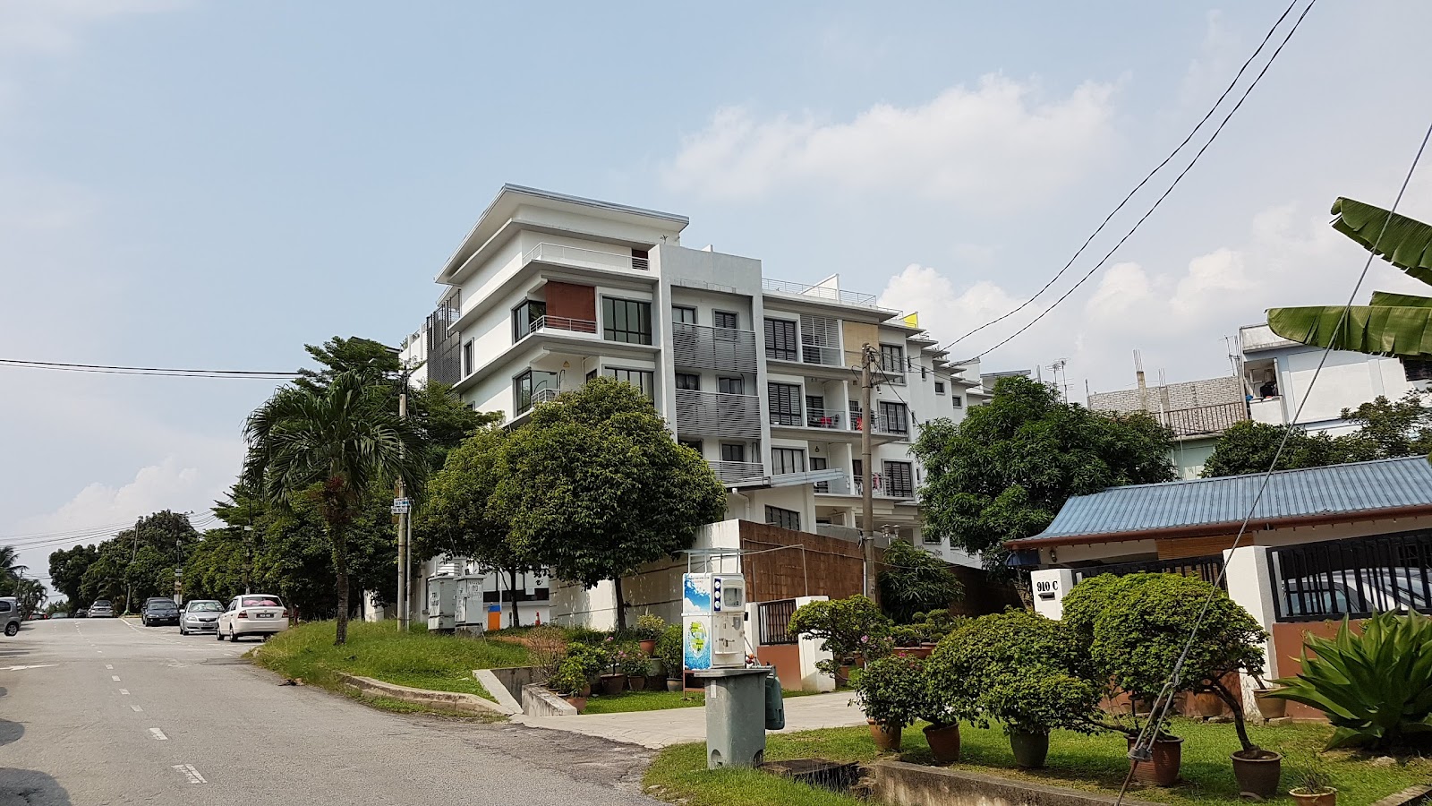 Laman Ara Utama: A multi-story residential apartment building viewed from the street, with cars, trees, and a smaller structure with a blue roof in the foreground.