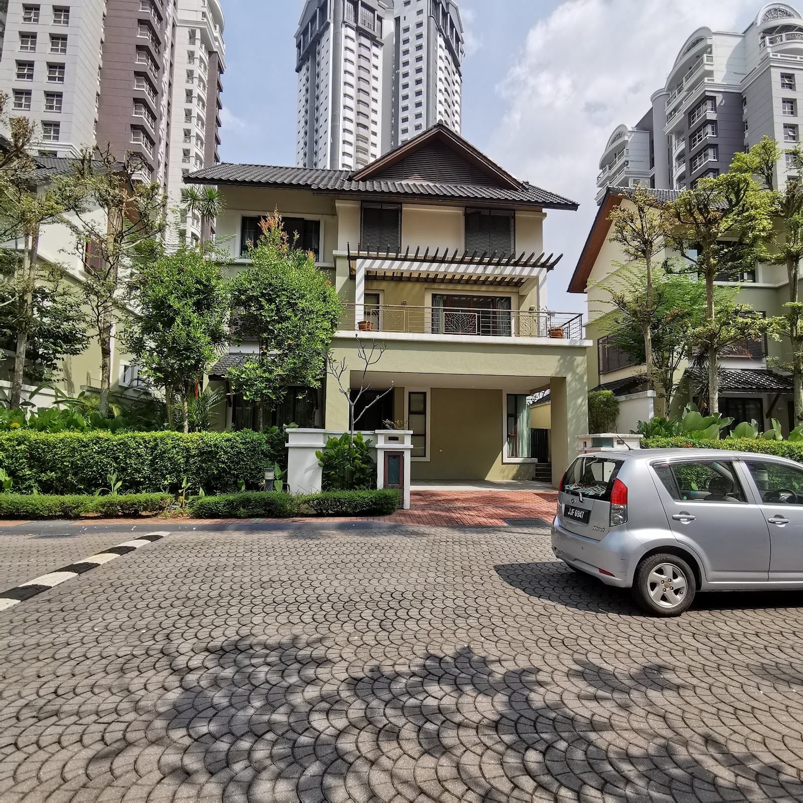 Almaspuri: A landed house within a gated residential development, with high-rise towers in the background and a car parked in the driveway