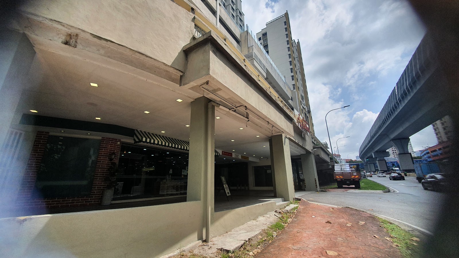 Serviced Residence @ Pelangi Damansara Sentral: Ground floor covered walkway of a building with retail units, under an elevated highway/flyover, with street traffic visible