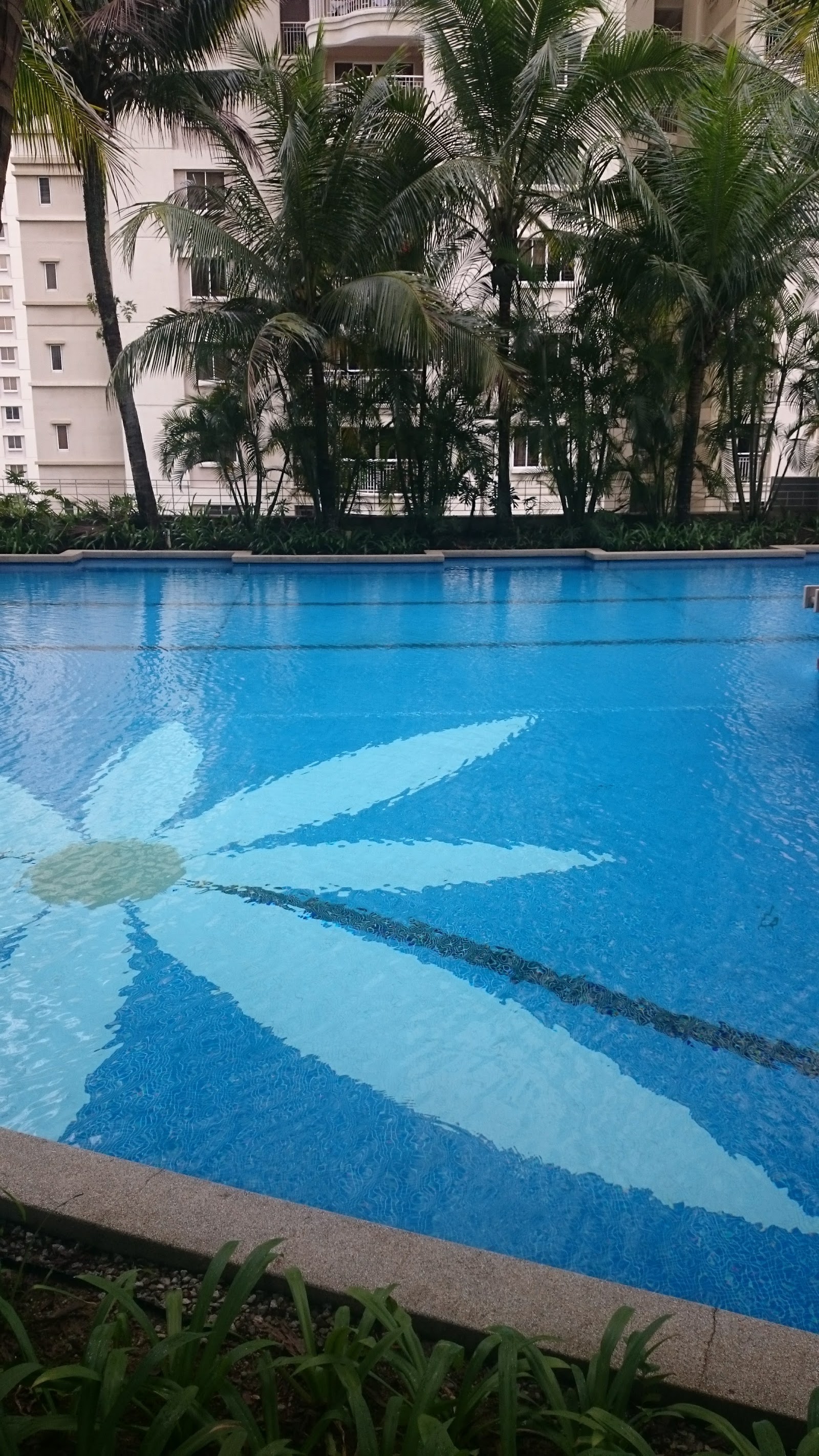 Kiaramas Sutera: Swimming pool with a decorative flower tile pattern, surrounded by palm trees and an apartment building