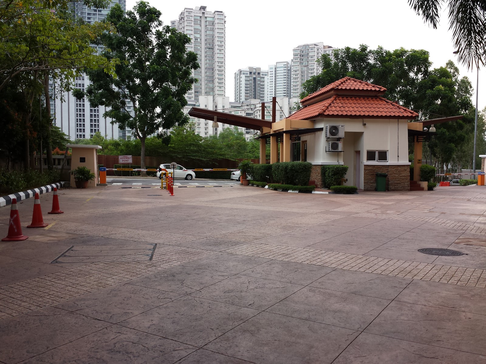 Hartamas Regency 2 Mont Kiara: Guardhouse entrance with red-tiled roof and boom gate, driveway, and traffic cones, with high-rise buildings visible in the background