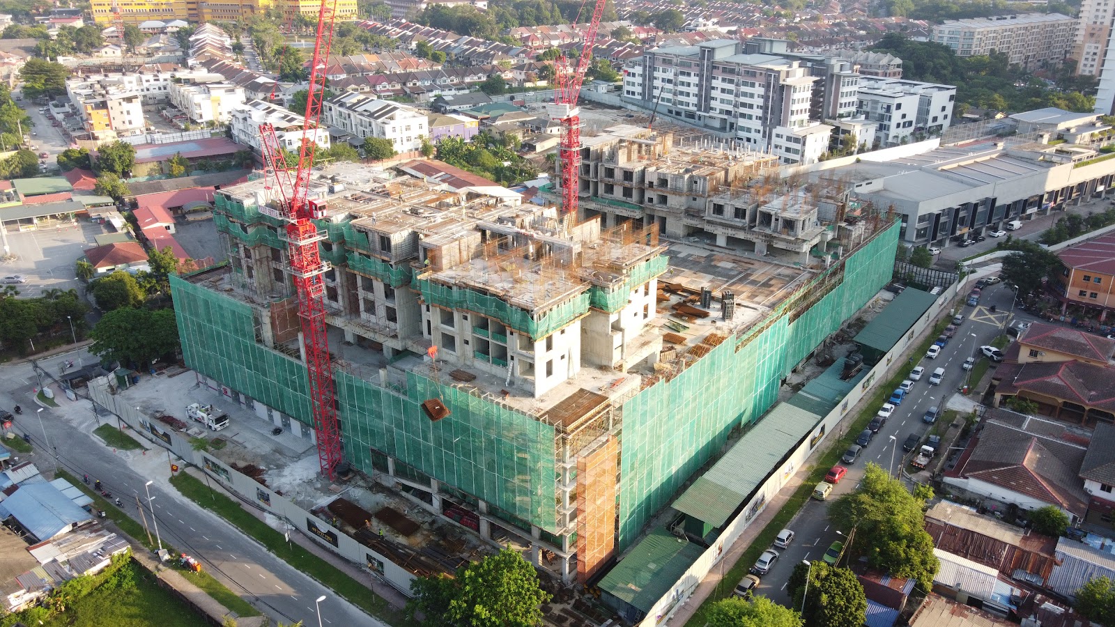 121 Residences: Aerial view of a high-rise building under construction, wrapped in green safety netting with cranes, surrounded by an urban residential neighborhood