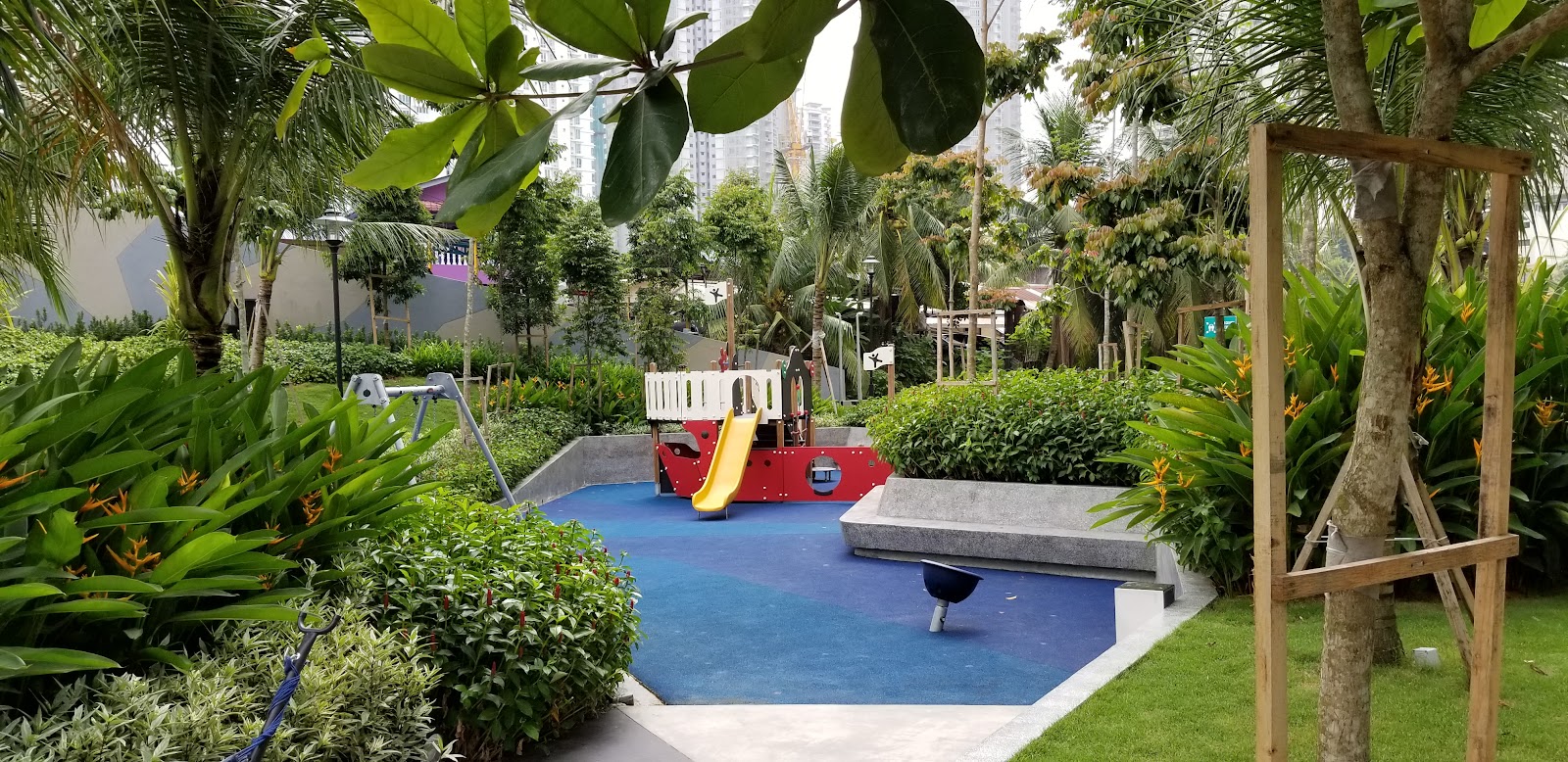 Residensi Sefina Mont Kiara: A children's playground with a slide and pirate ship structure on blue rubber flooring, surrounded by lush landscaping