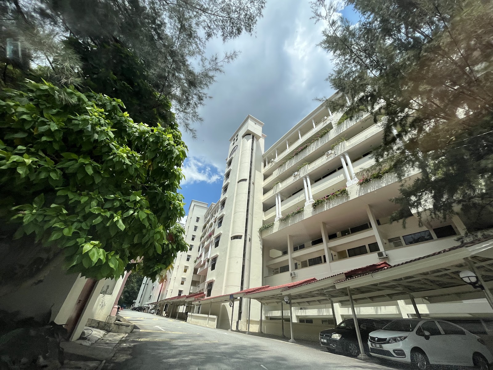 Tivoli Villas: Exterior view of a residential apartment building with balconies, seen from a driveway with trees and parked cars in a covered parking area
