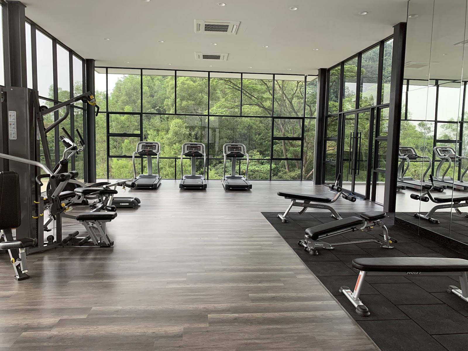 Secoya Residences @ Pantai Sentral Park: A gym with treadmills, exercise machines, and benches facing floor-to-ceiling windows overlooking greenery