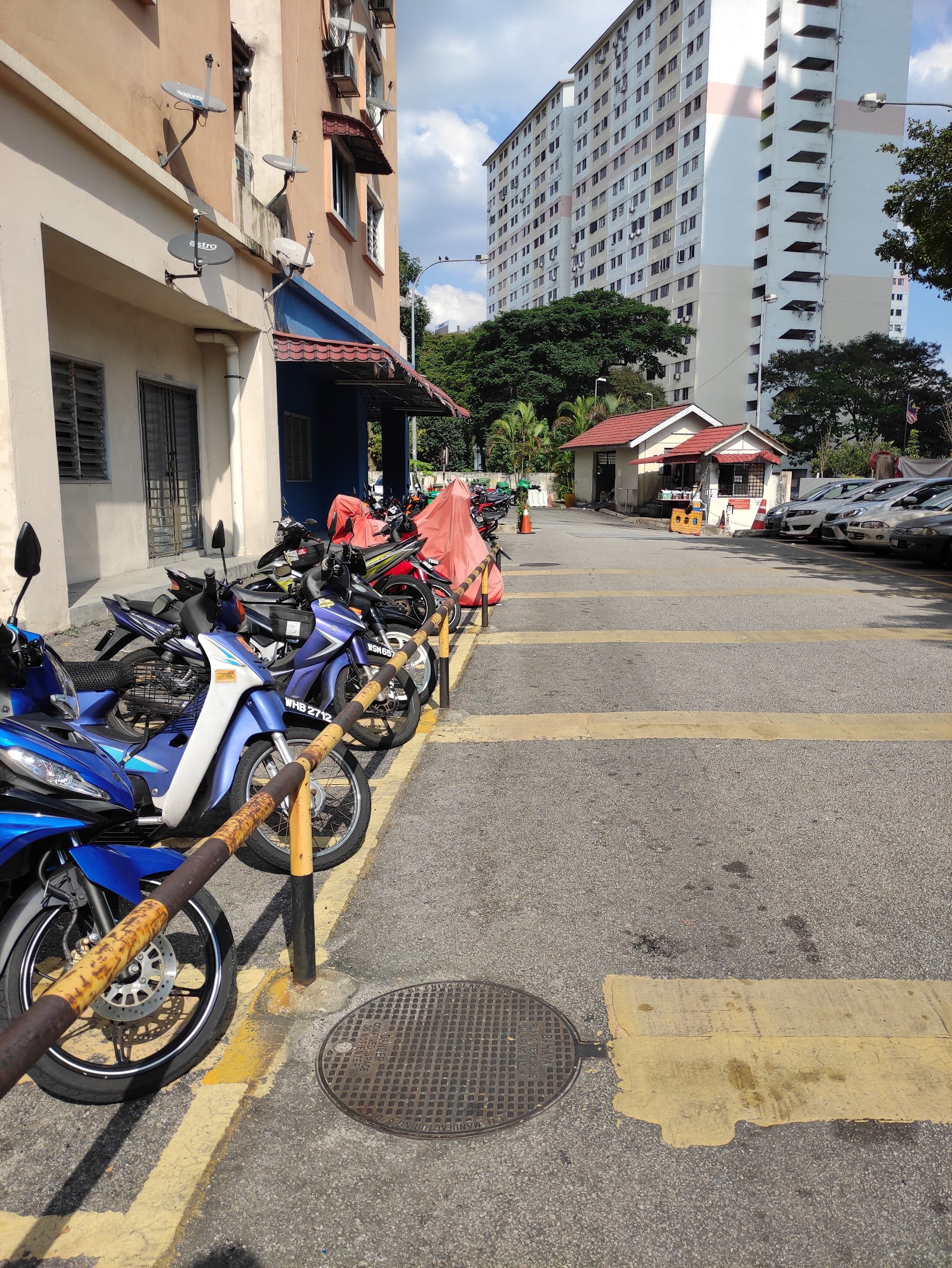 Pangsapuri Pelangi Ara: Motorcycles parked along a road beside residential buildings, with cars parked further down and high-rise towers in the background