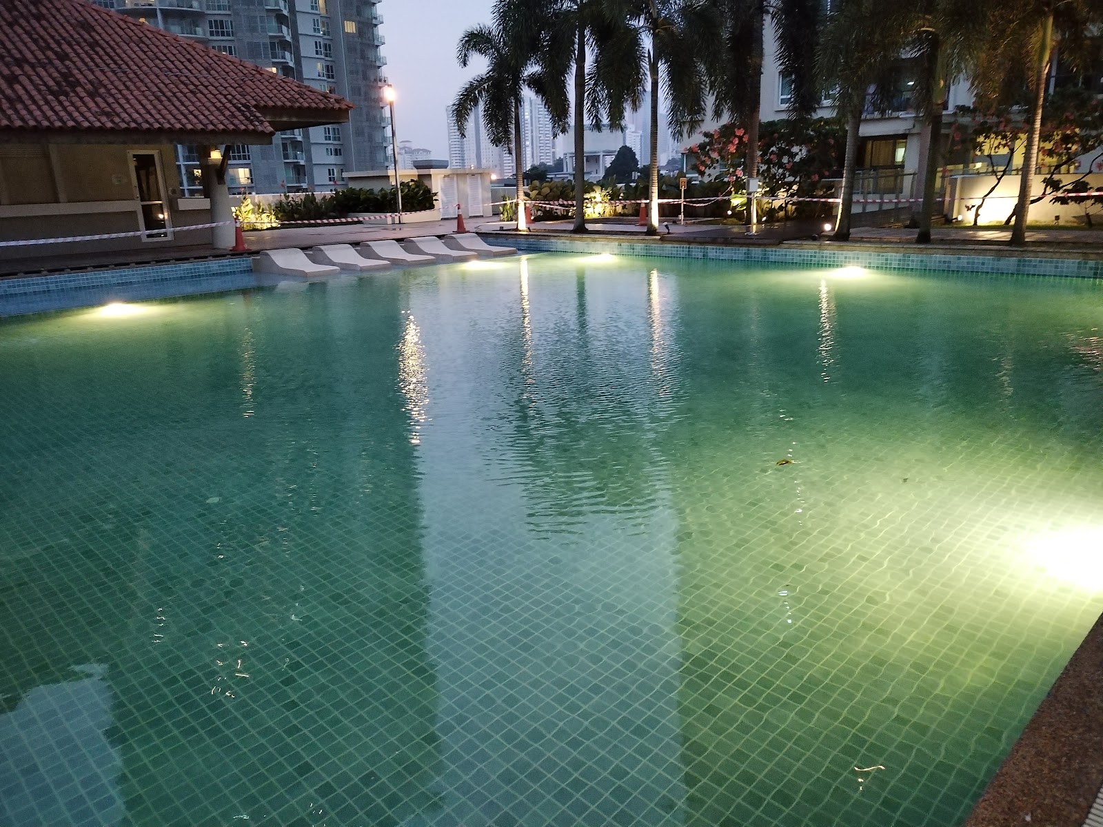 Mont Kiara Banyan: An outdoor swimming pool with underwater lights, lounge chairs, surrounded by palm trees and residential towers at dusk