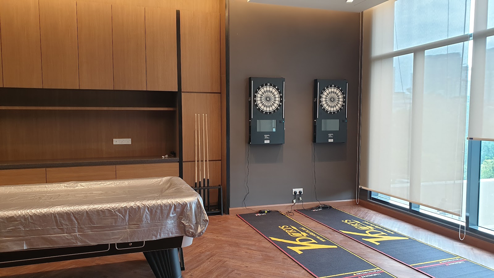 Residensi Solaris Parq: A recreation room with a covered pool table, cue rack, two electronic dartboards on the wall, and roll-up window shades
