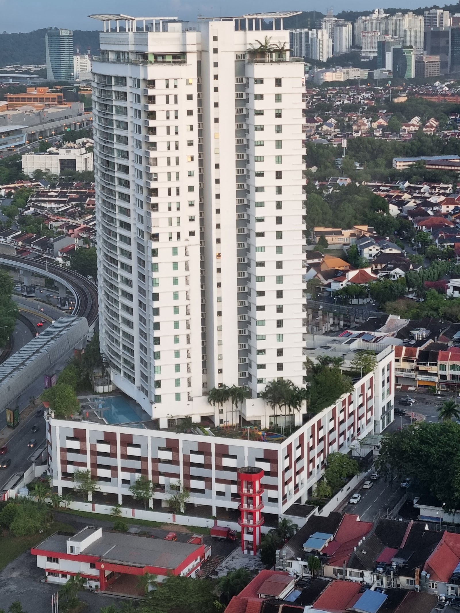 Sinaran TTDI: Aerial view of a tall white residential tower with a low-rise podium and pool, surrounded by suburban houses and a train line
