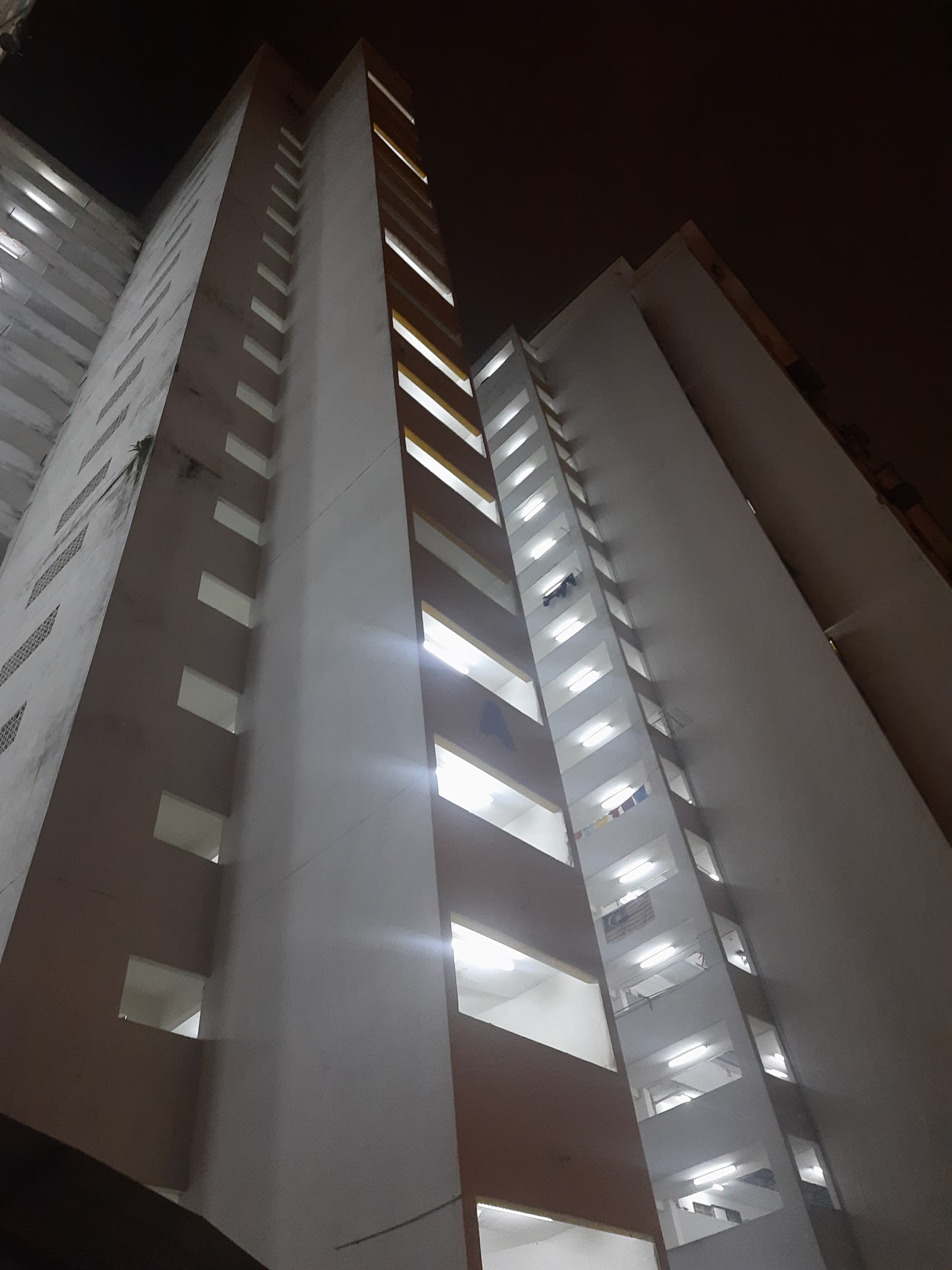 PPR Pantai Ria: Night view looking up at tall residential apartment towers with lit windows and corridors