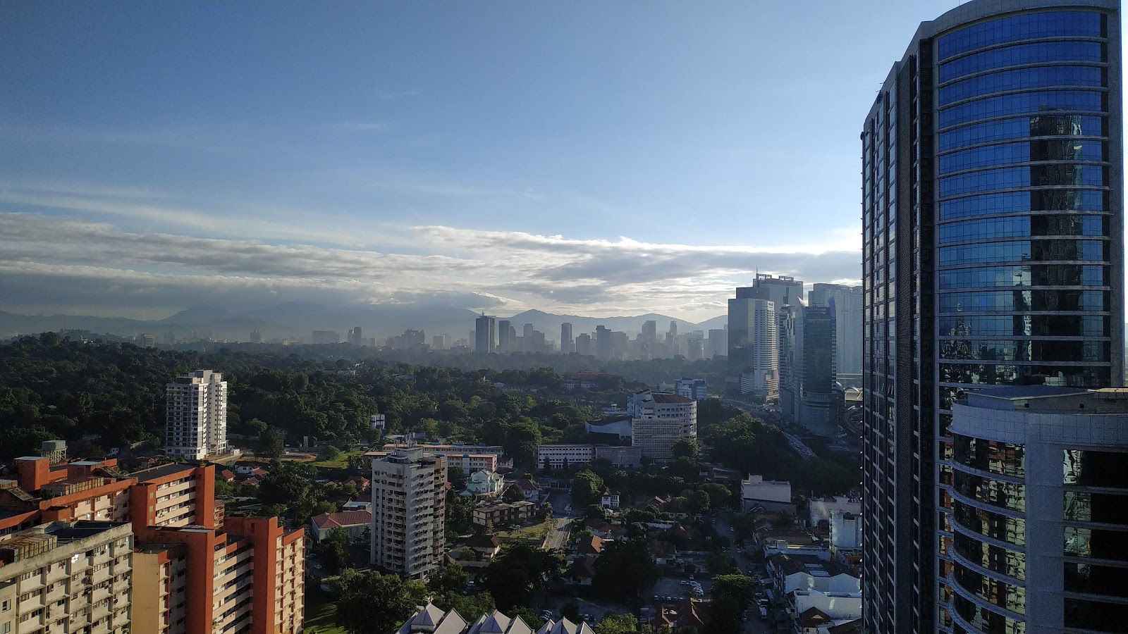 Gaya Bangsar: Panoramic cityscape view from a high-rise showing surrounding buildings, greenery, and mountains in the distance under a partly cloudy sky