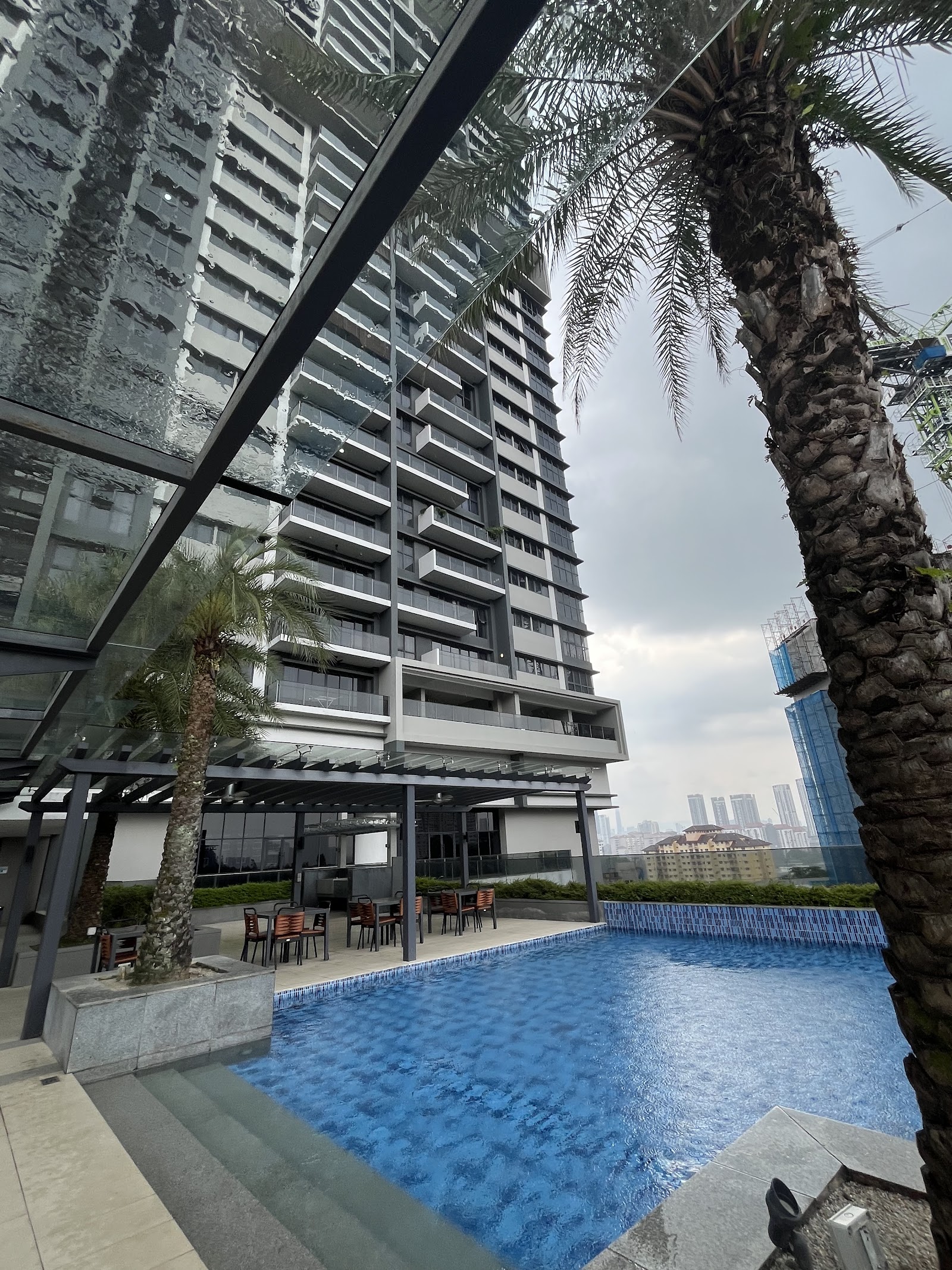 Secoya Residences @ Pantai Sentral Park: Rooftop swimming pool with palm trees and lounge seating area, overlooking the high-rise tower and city skyline