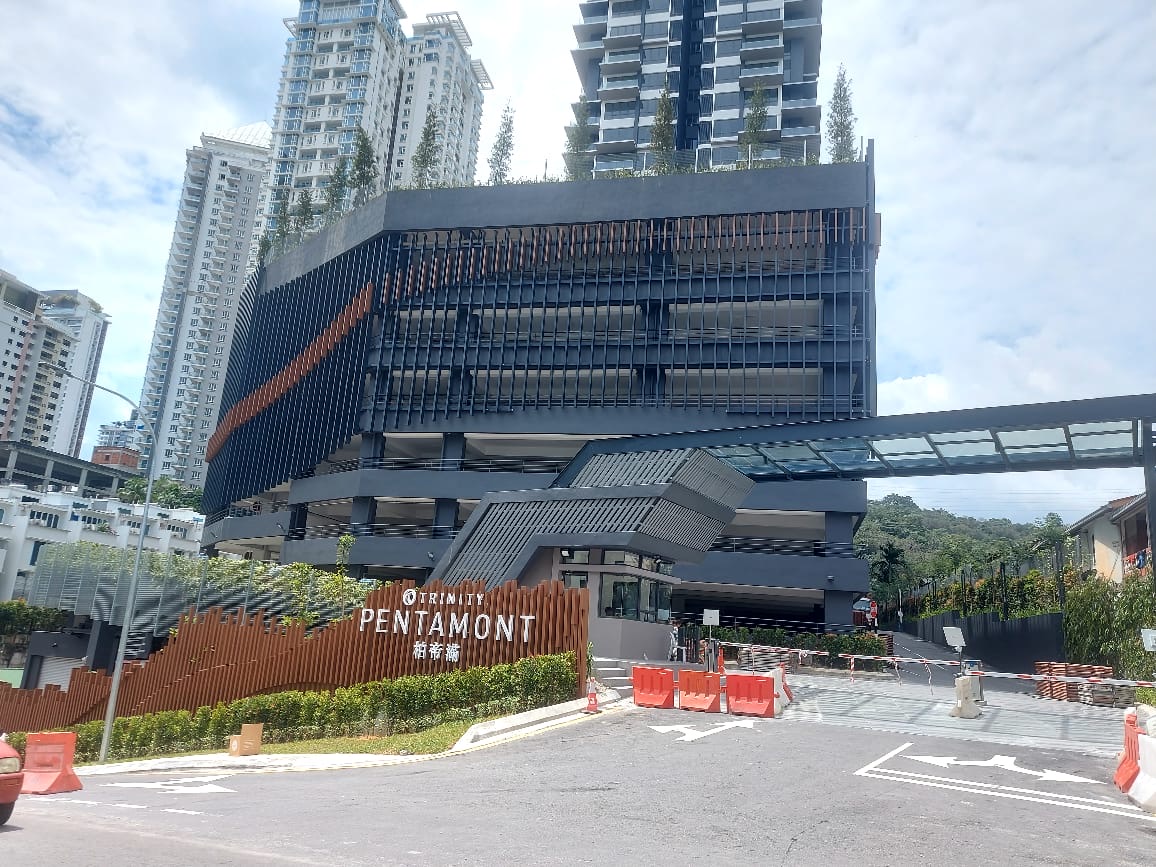 Trinity Pentamont: Street-level view of the Trinity Pentamont development, showing its multi-story podium with a skybridge, entrance signage, and residential towers behind it.