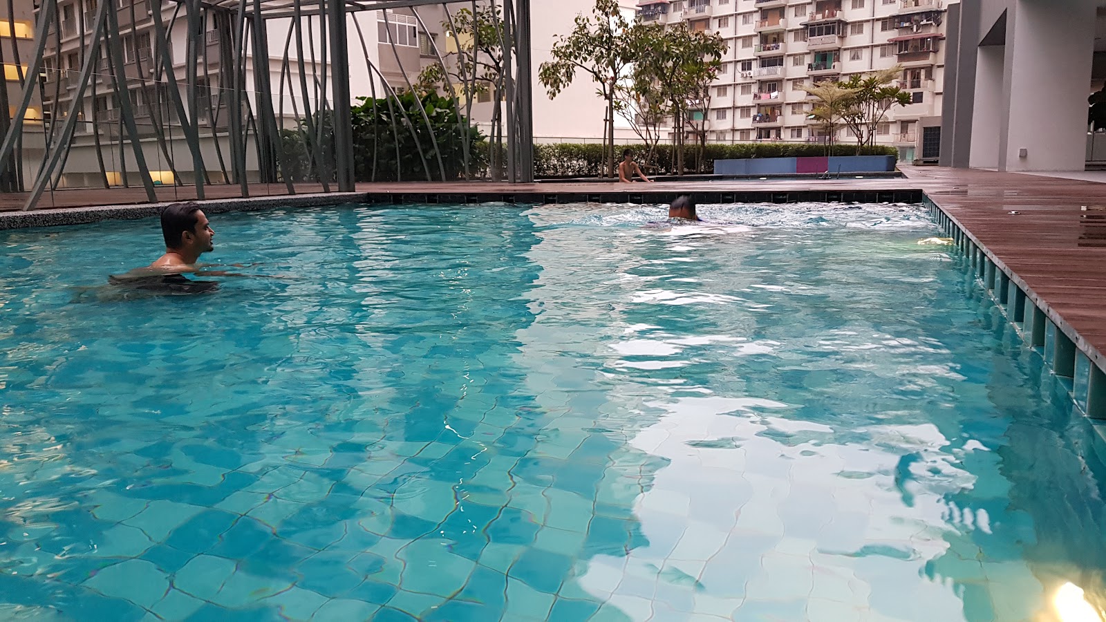 KL Gateway Residences: People swimming in an outdoor rooftop swimming pool with a wooden deck, surrounded by residential apartment buildings