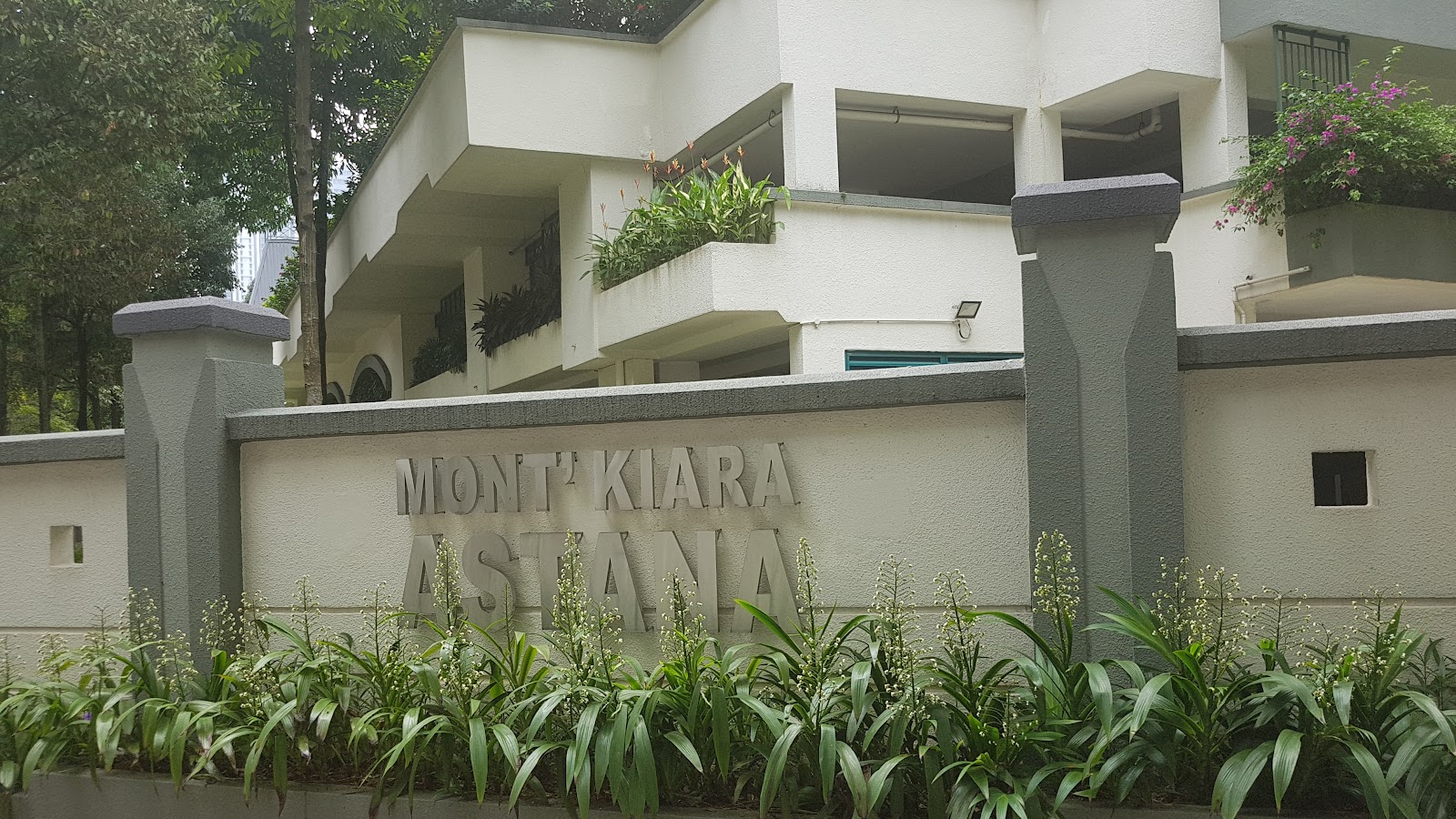 Mont Kiara Astana: Entrance wall with the development's name carved into it, with the building facade and balconies visible behind, surrounded by greenery