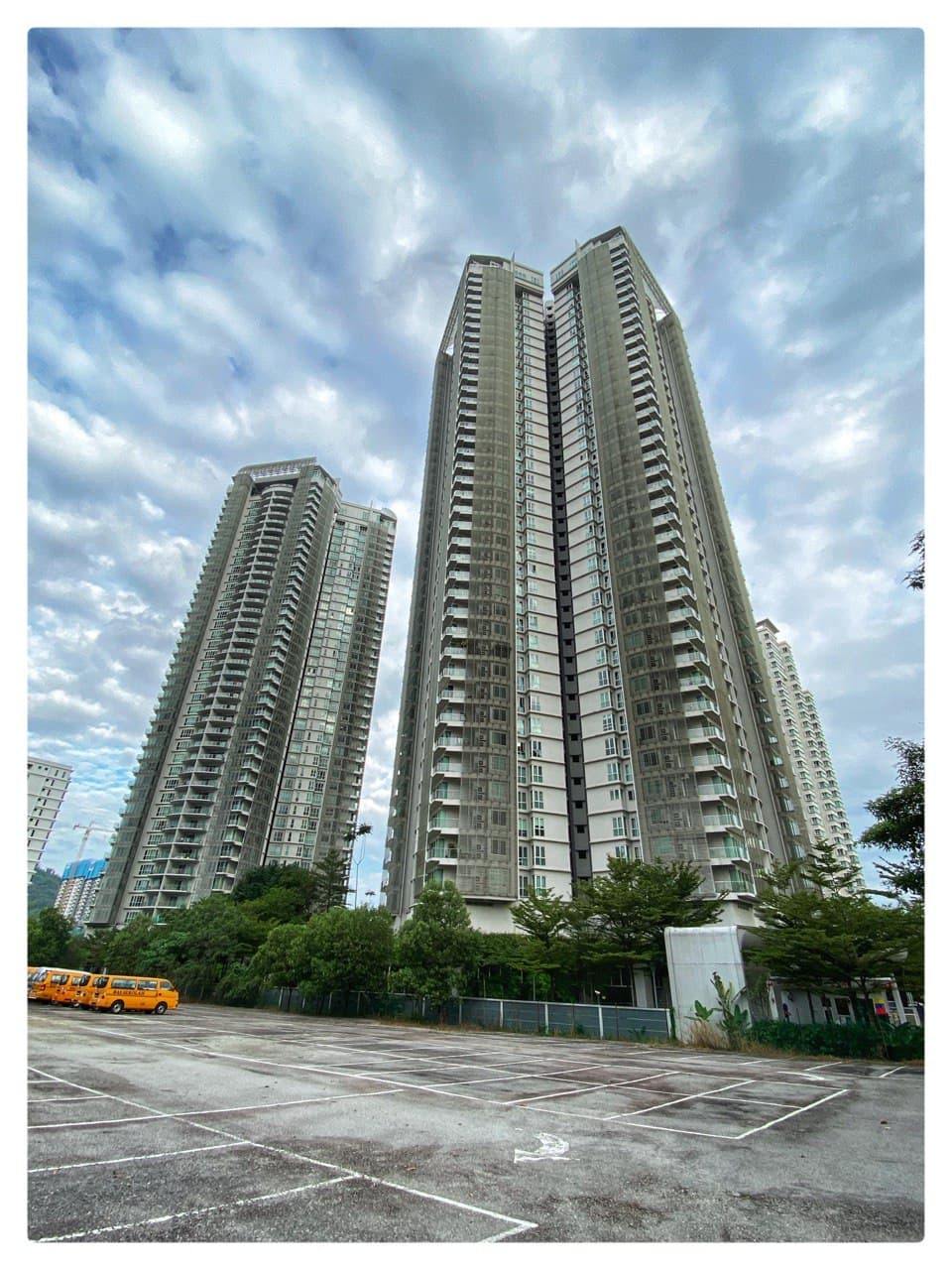 28 Mont Kiara: Two tall residential towers viewed from a parking lot with trees and buses