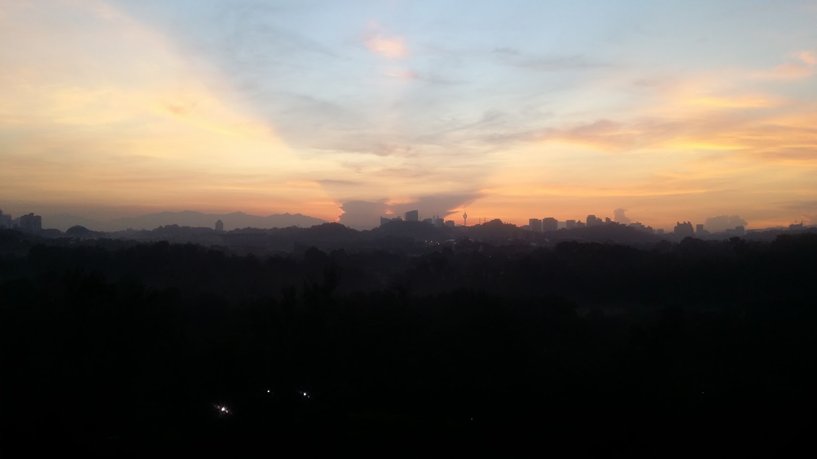 The Residence Condominium @ TTDI: Twilight skyline view with city buildings silhouetted against an orange and blue sunset sky, seen from an elevated vantage point with trees in the foreground