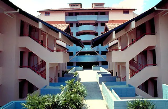 Trellises: Courtyard view of a multi-story residential building with red railings, staircases, and covered walkways converging toward a central atrium with landscaped planters