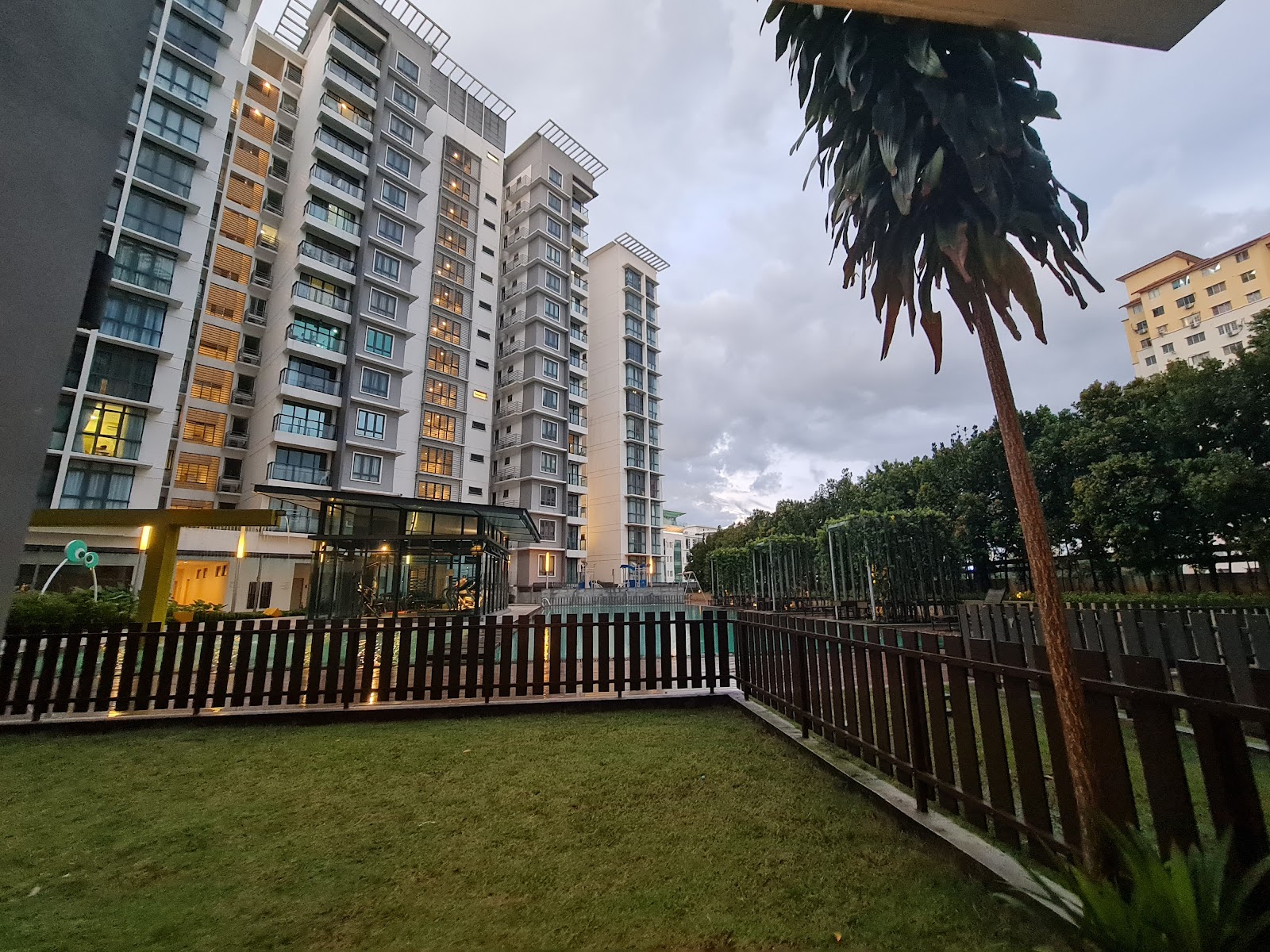Boulevard Residence: Evening exterior view of high-rise residential towers with a pool area, garden, and fencing in the foreground