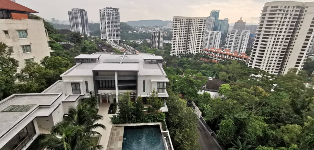 Bangsar Peak: Aerial view of a low-rise white house/villa with pool, surrounded by dense greenery and a skyline of high-rise condominium towers in the background