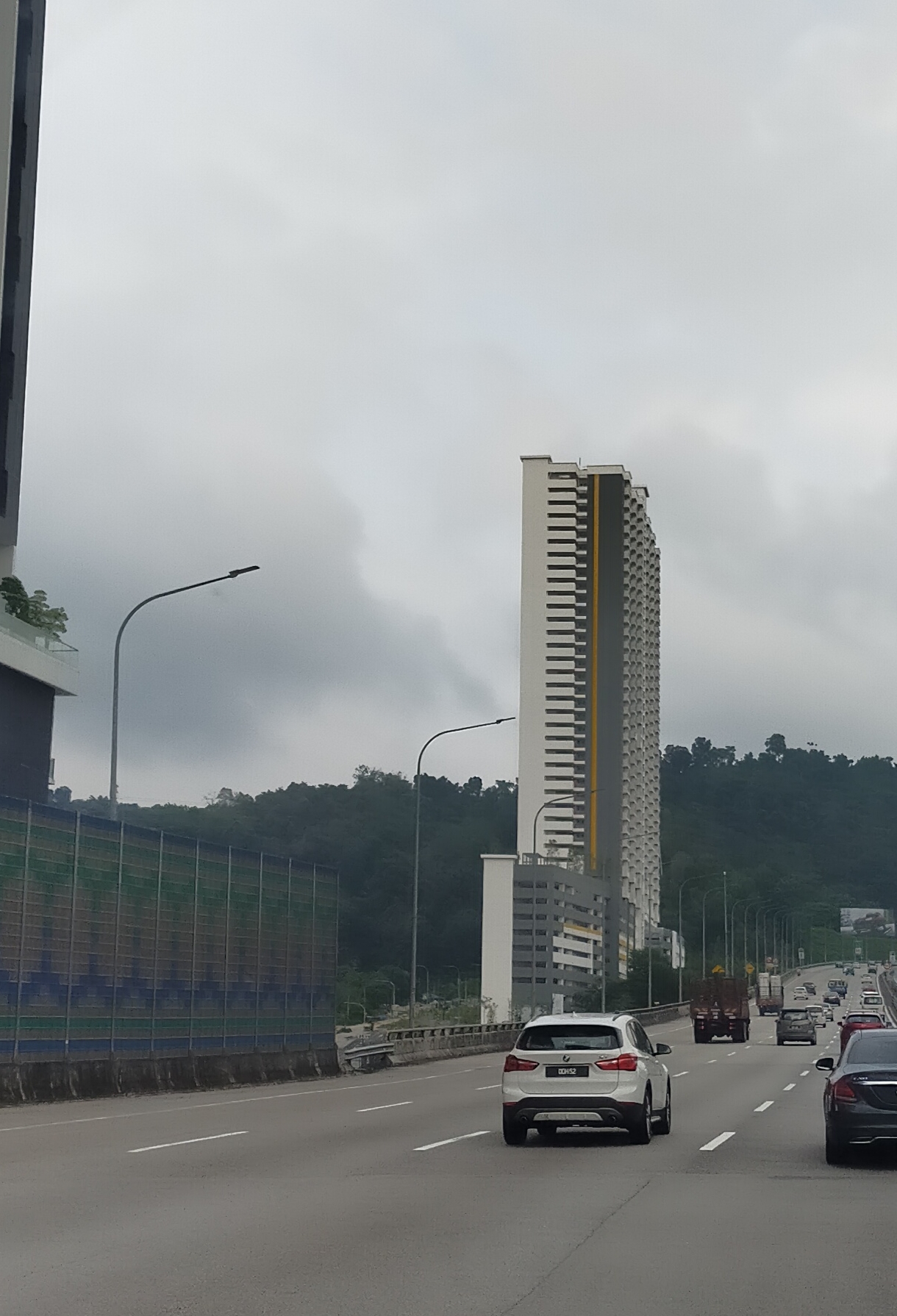 Kiara Kasih: A high-rise residential tower viewed from a highway with cars driving in the foreground