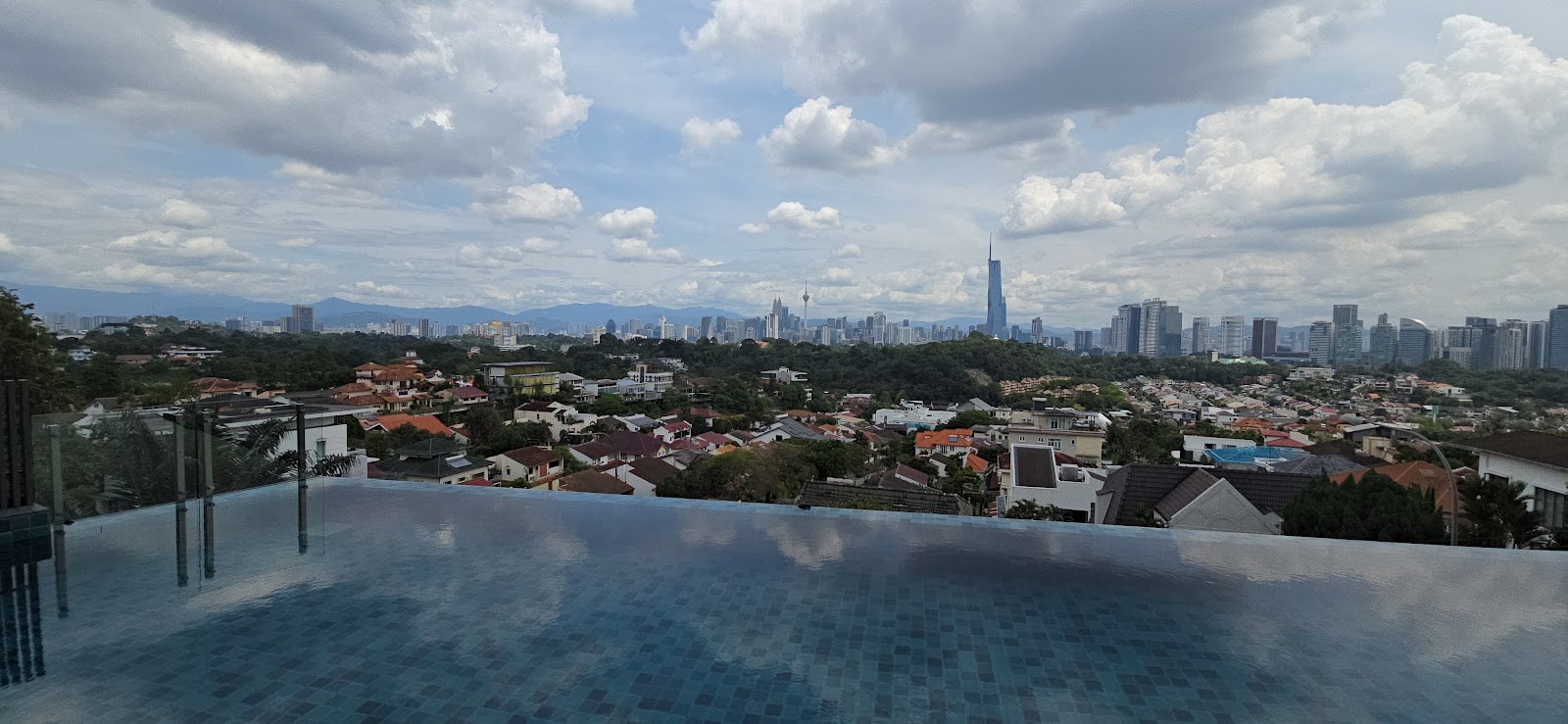 Rhombus @ Bangsar: Skyline view from an infinity pool edge showing Kuala Lumpur city buildings and towers including KL Tower and a tall skyscraper, with residential rooftops in the foreground