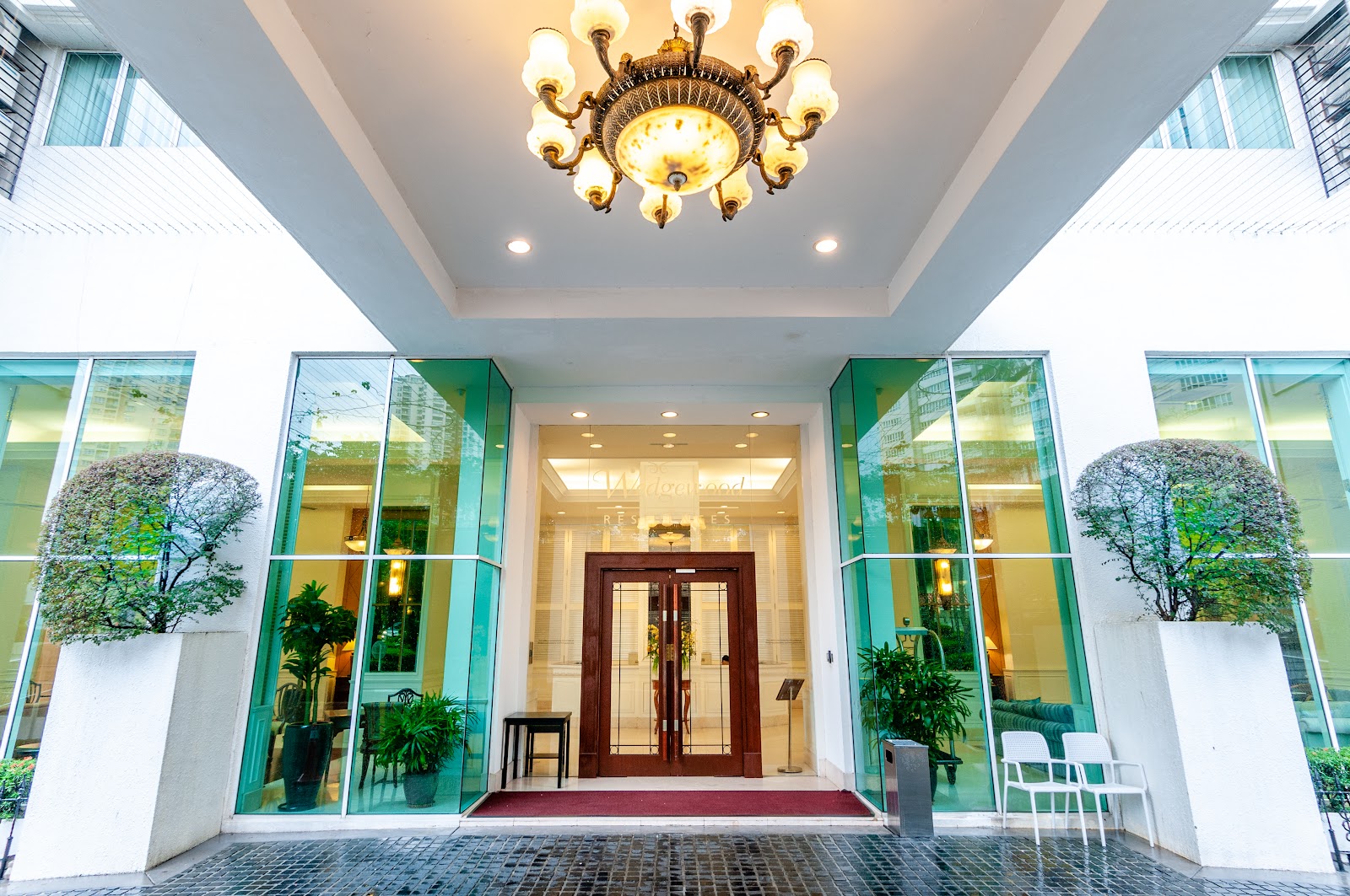Wedgewood Residences: Entrance facade of a residential building with glass canopy, chandelier, potted plants, and wooden double doors leading to a lobby