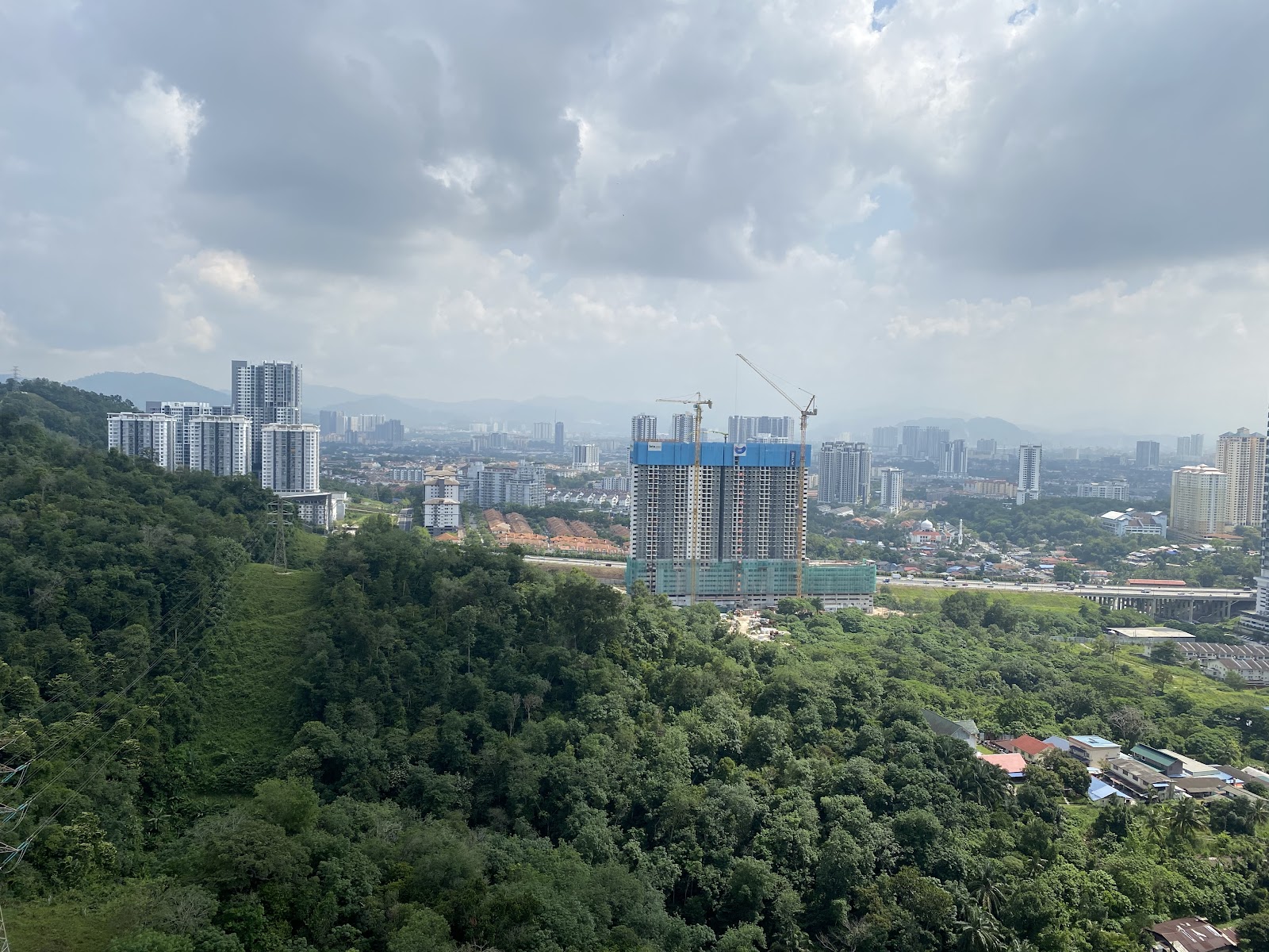 Sunway Mont Residences: Aerial cityscape view showing a high-rise under construction surrounded by trees, other buildings, and distant hills