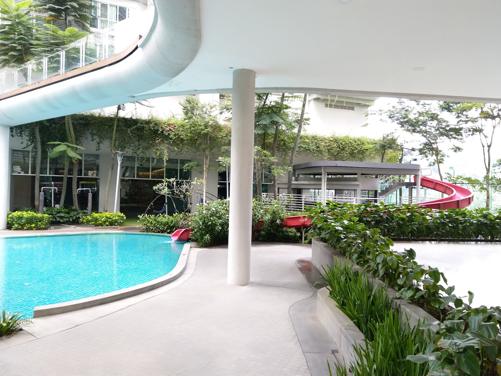 28 Mont Kiara: Swimming pool area with a red water slide, surrounded by lush greenery under a covered walkway