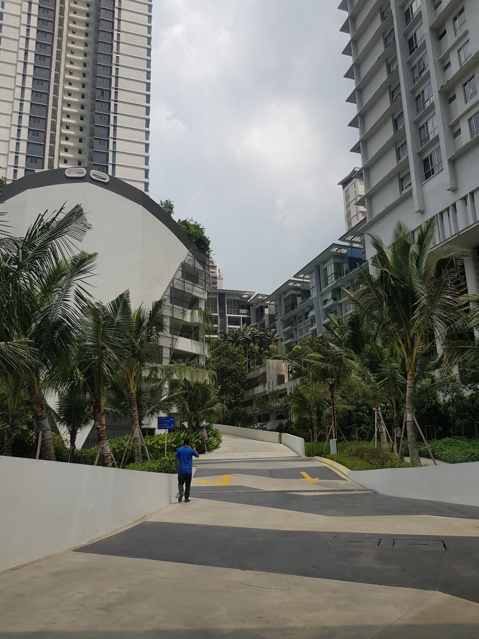 Residensi Sefina Mont Kiara: View of a residential complex driveway lined with palm trees, with high-rise apartment towers in the background and a person walking on the road