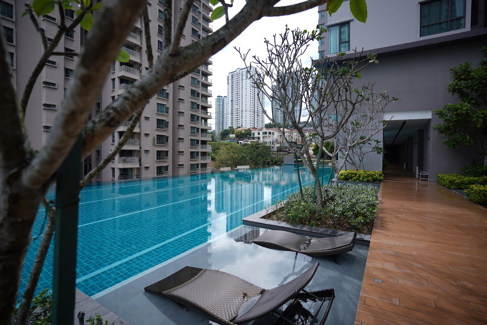 Sunway Mont Residences: An infinity-edge swimming pool with lounge chairs on a wooden deck, surrounded by trees and high-rise buildings in the background
