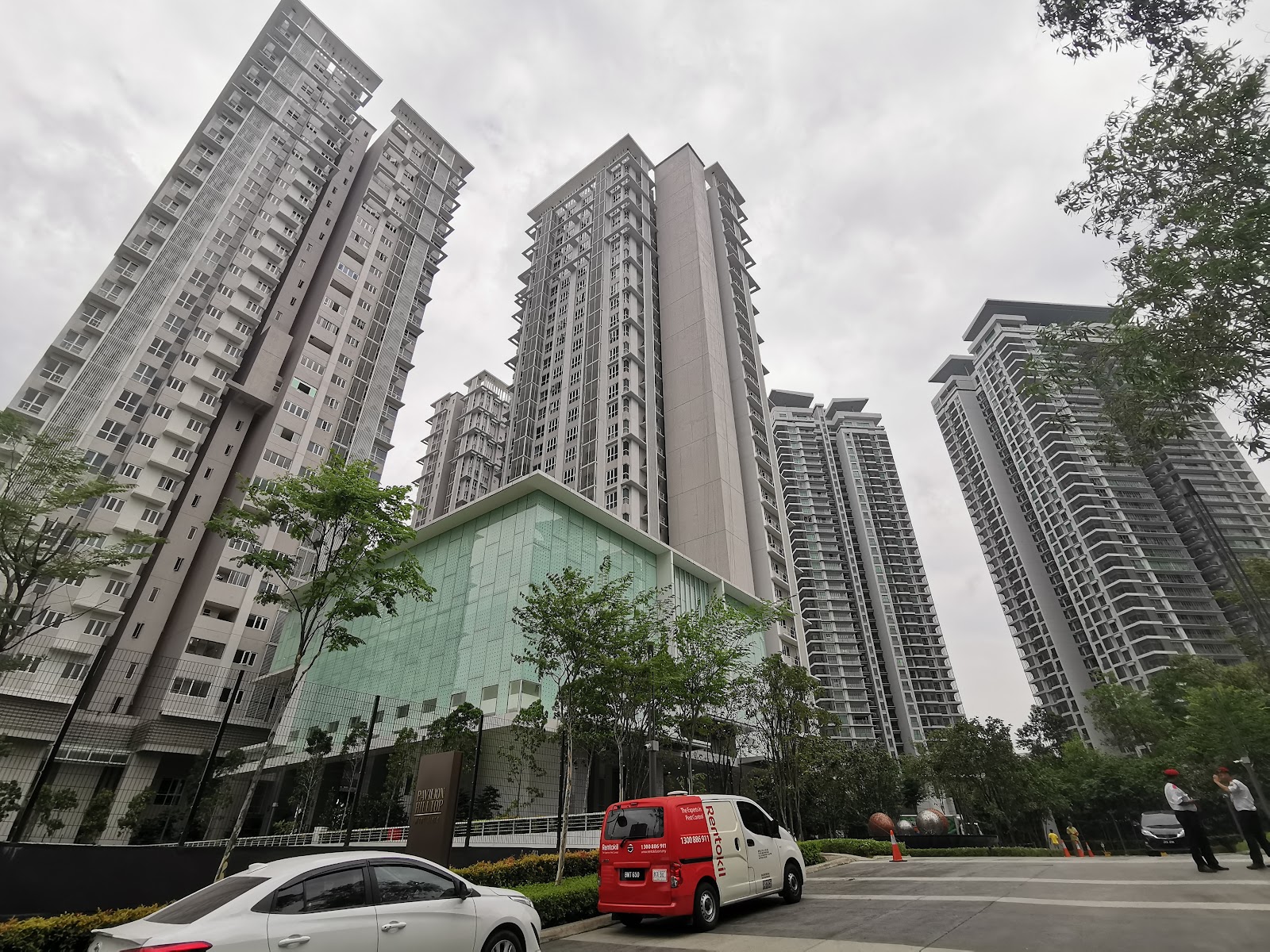 Pavilion Hilltop: High-rise residential towers viewed from ground level with vehicles and pedestrians in the courtyard