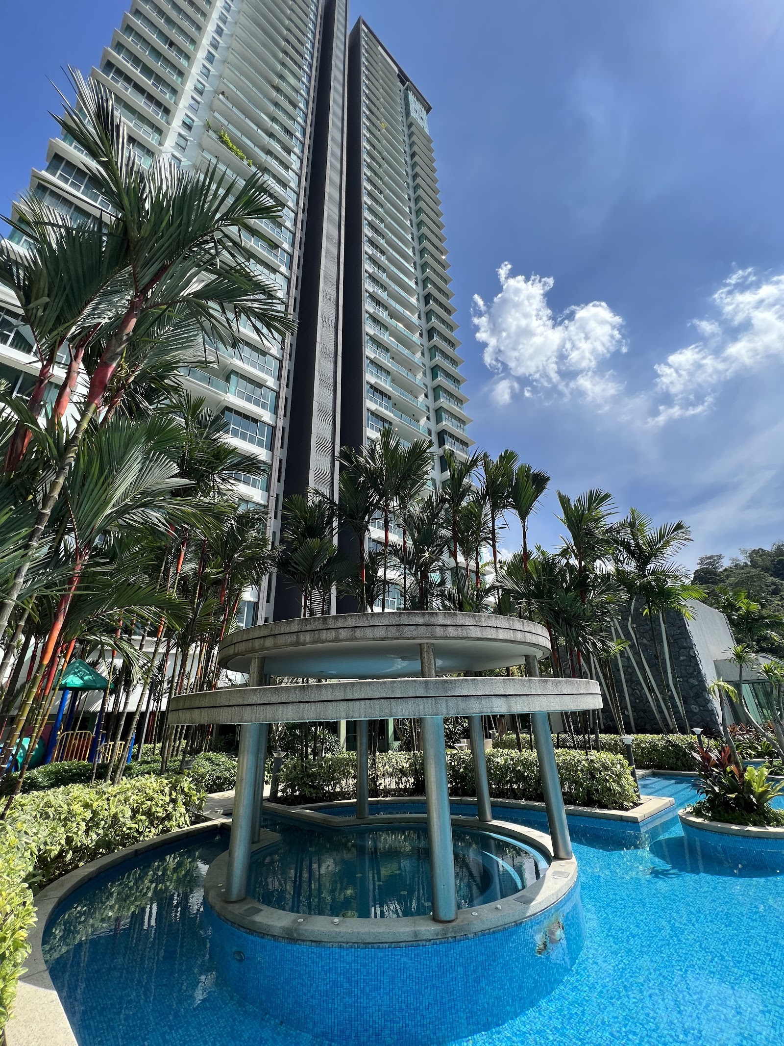 Kiaramas Cendana: Outdoor swimming pool with a circular water feature/fountain structure, surrounded by palm trees and high-rise residential towers