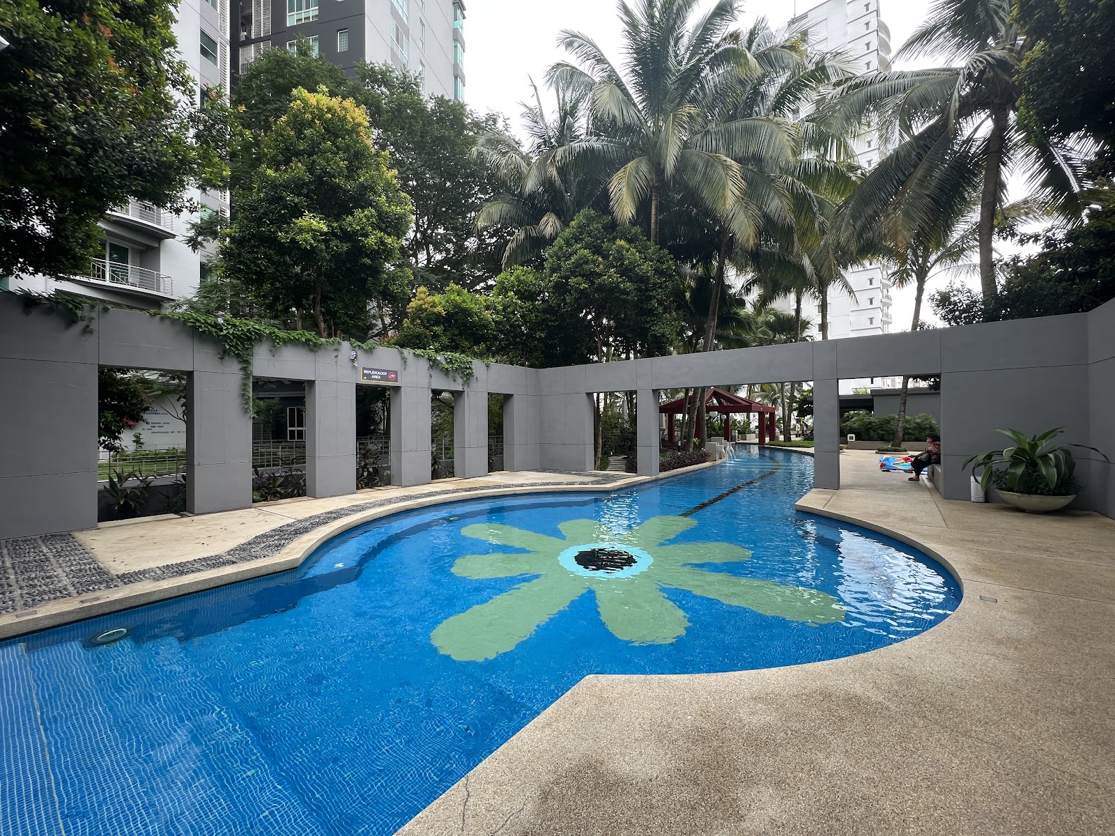 Kiaramas Ayuria: Swimming pool with a decorative flower mosaic design, surrounded by a walled courtyard, palm trees, and a red gazebo, with residential towers in the background