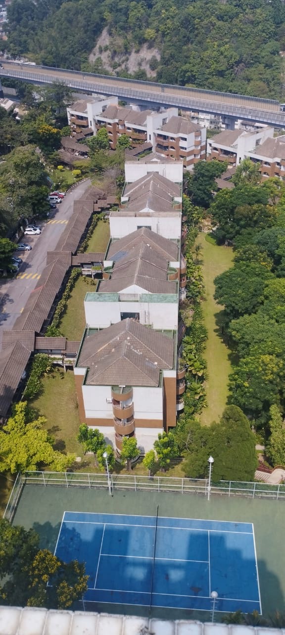 Bangsar Puteri: Aerial view of a low-rise residential building complex with tiled roofs, surrounded by trees and a tennis court, adjacent to a road