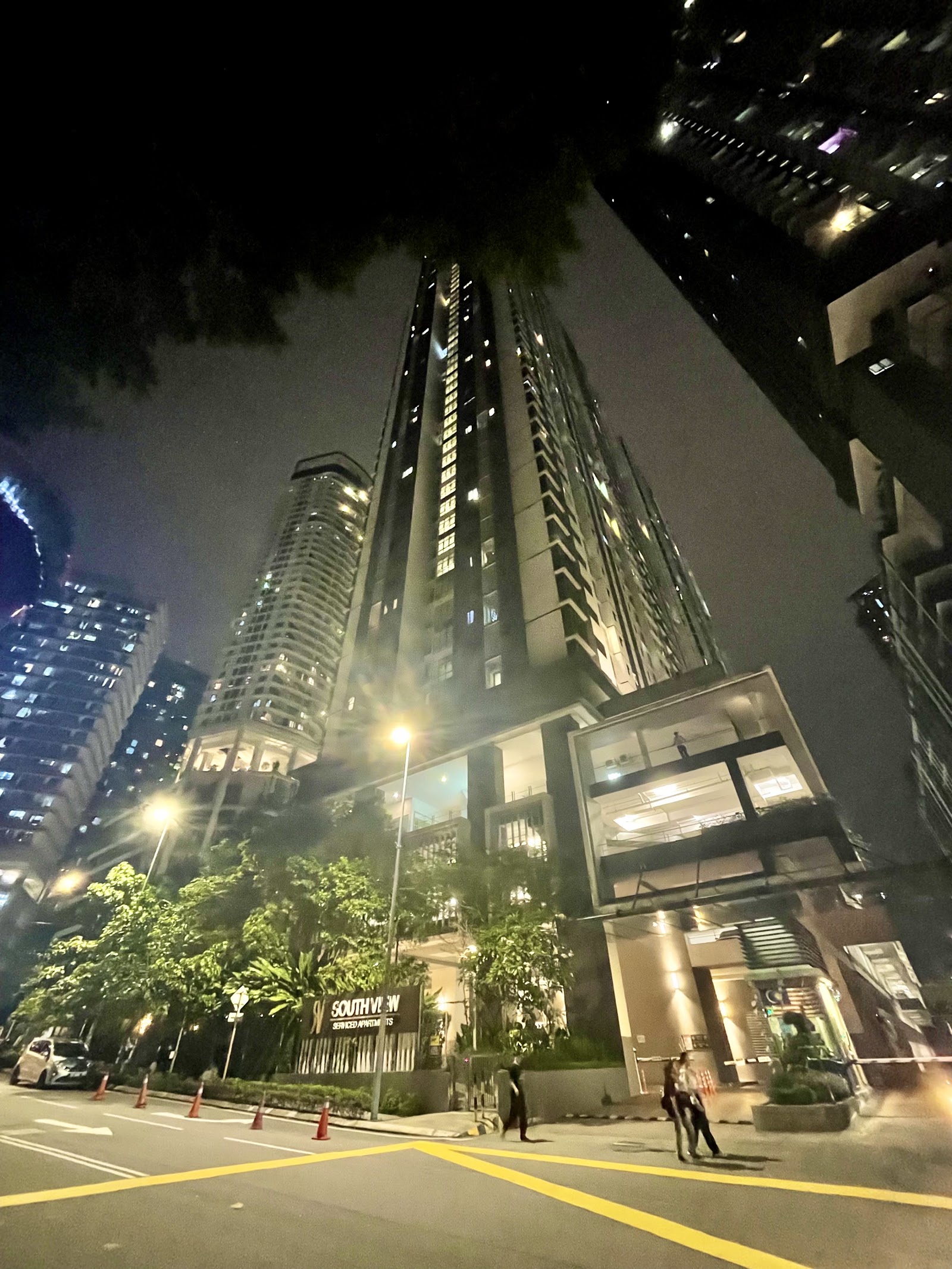 South View: Night view of a tall residential tower called South View, with street, cars, pedestrians, and other nearby buildings visible