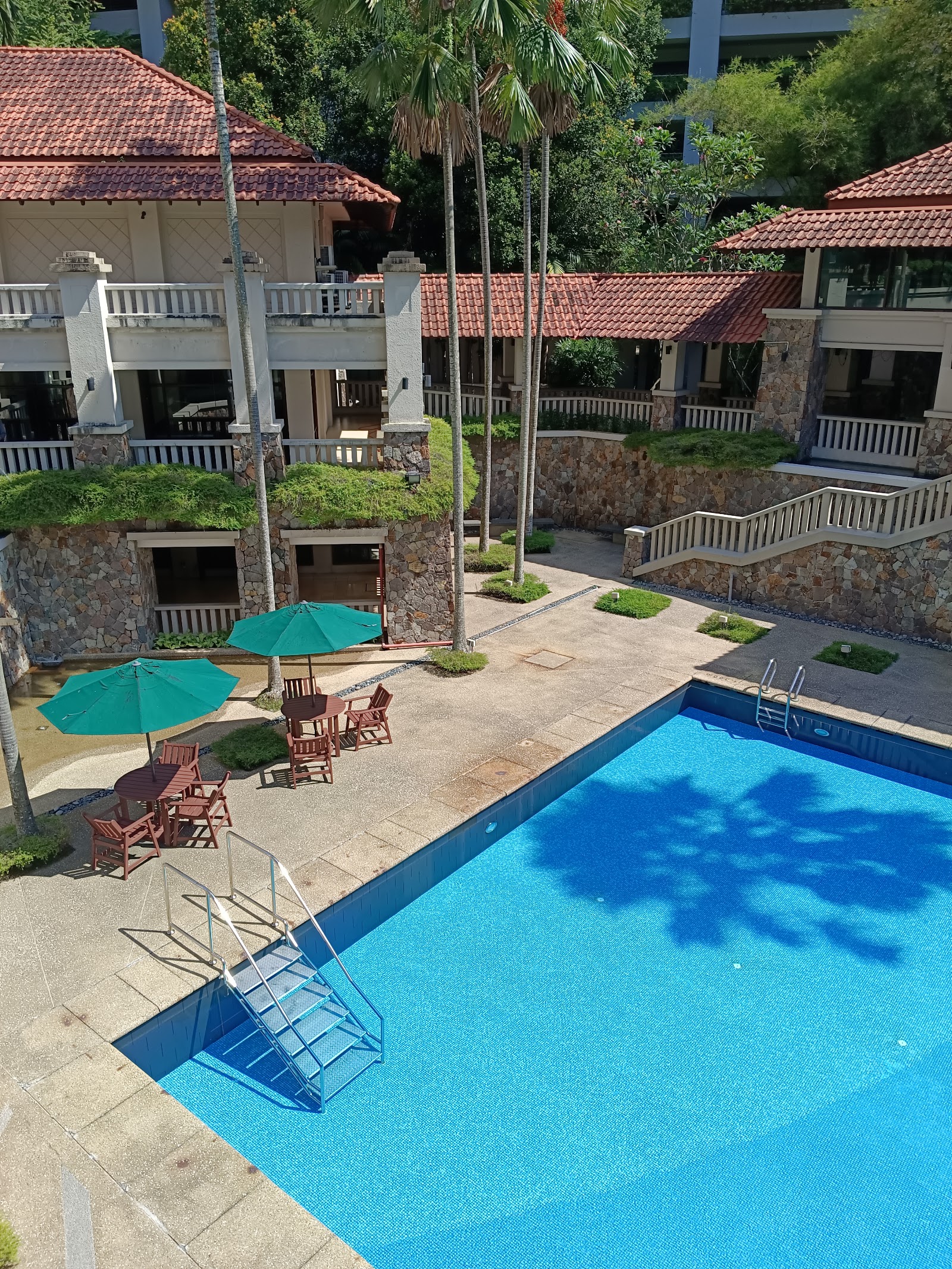 Mont Kiara Damai Resort Condominium: Swimming pool with pool ladder and steps, surrounded by terrace with umbrellas, chairs and tables, overlooked by resort-style condo buildings with terracotta roofs
