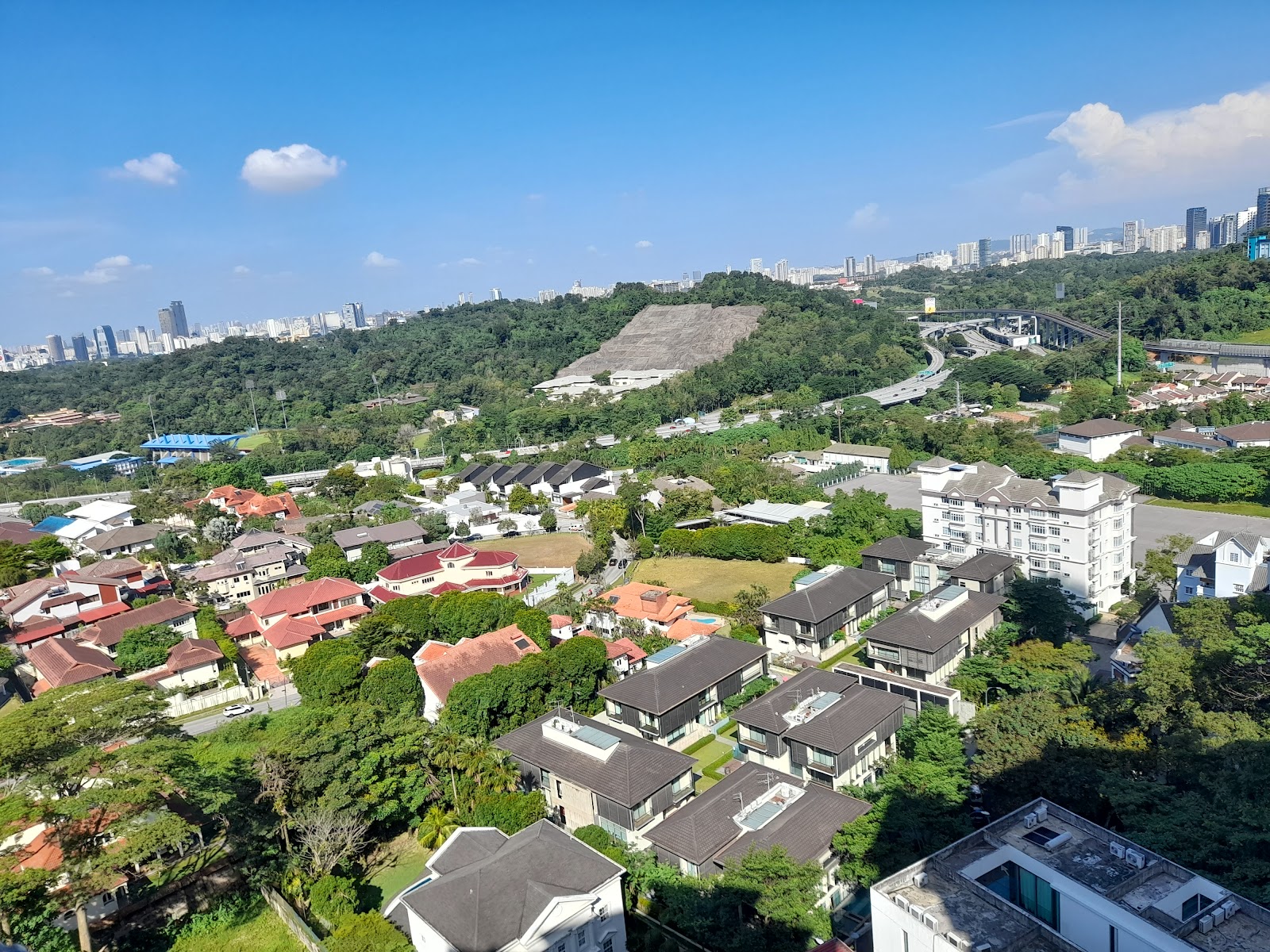 Contessa: Aerial view from a high-rise development overlooking landed housing, greenery, a highway and city skyline in the distance