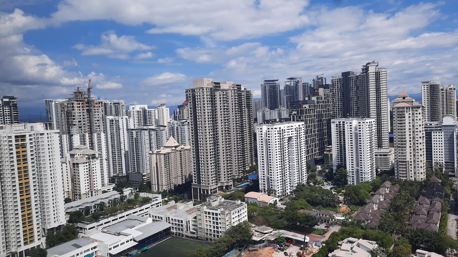 Gateway Kiaramas: Aerial view of a dense cluster of high-rise residential towers under a partly cloudy sky, with a construction crane visible among the buildings