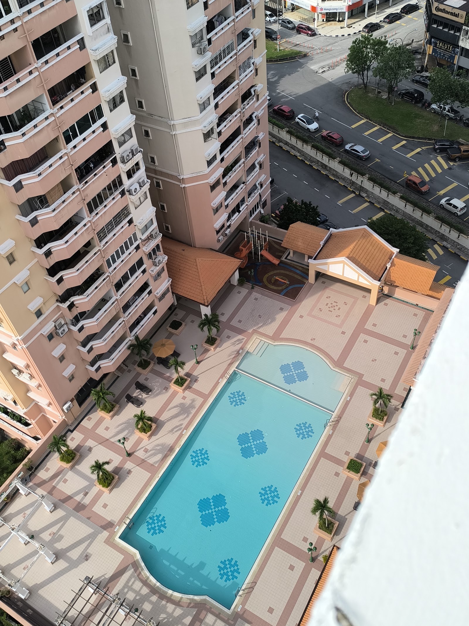 Sri TTDI: Aerial view of the swimming pool, sun deck, and gazebo shelters within the condominium grounds, with the tower blocks and street below visible