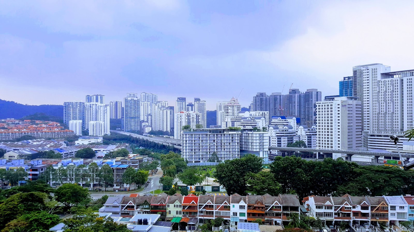 Menara Hartamas: Cityscape view from a high vantage point showing numerous high-rise towers, low-rise houses, and greenery under a cloudy sky